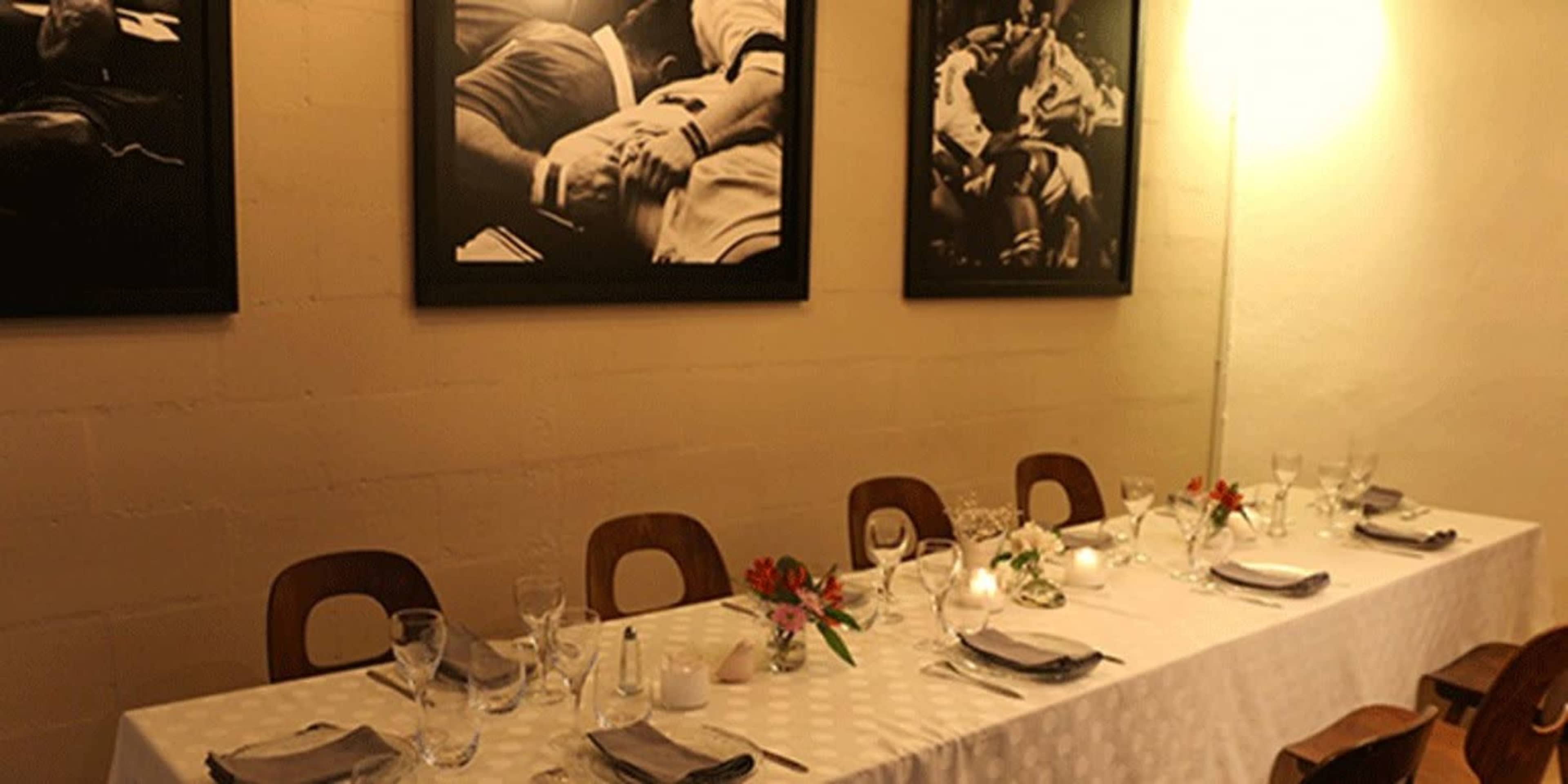 A long dining table is set with glasses and flowers under black and white wall photographs in a softly lit restaurant.