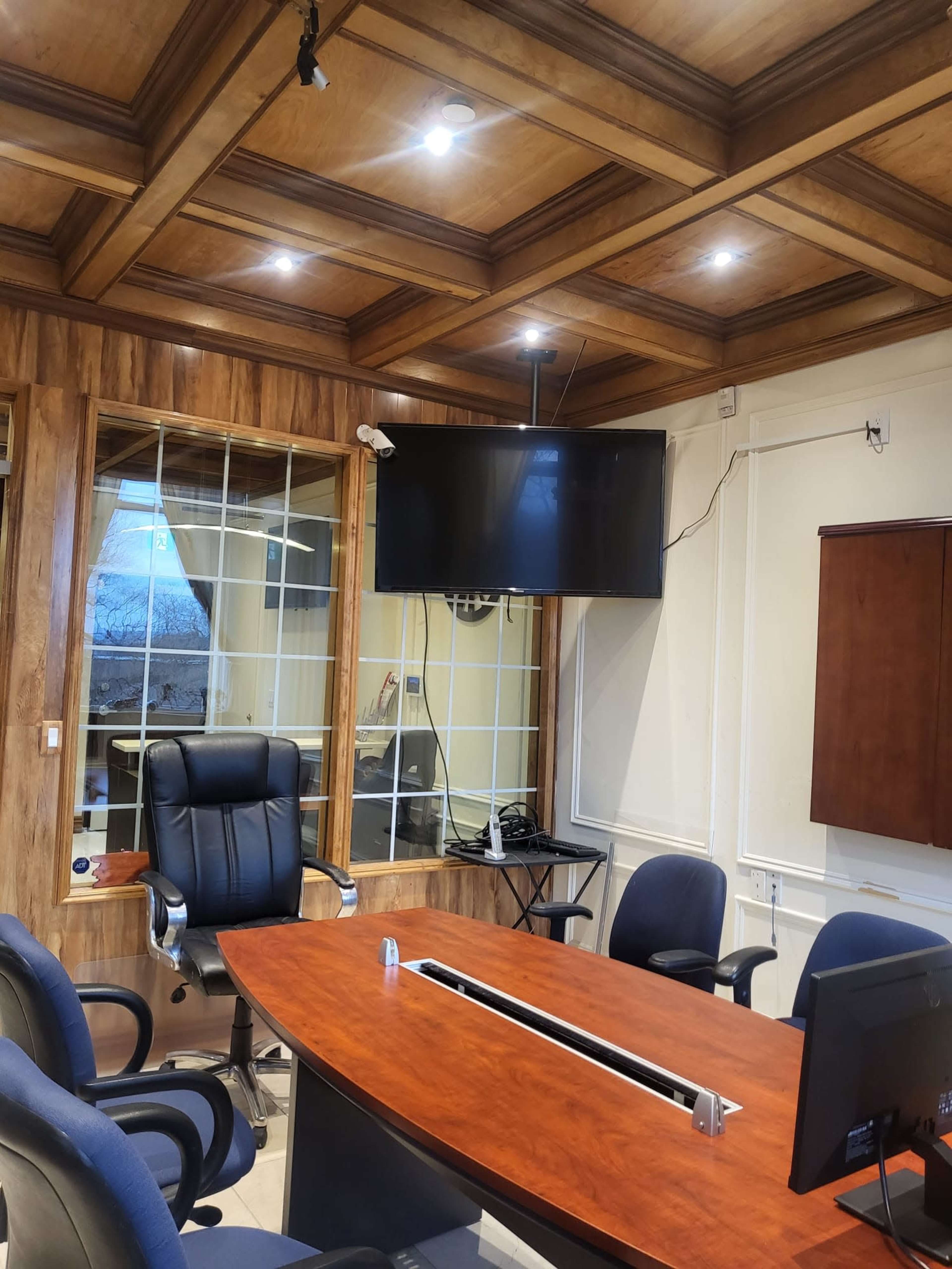 The image shows a conference room with a wooden ceiling, a large table, several chairs, and a wall-mounted TV.