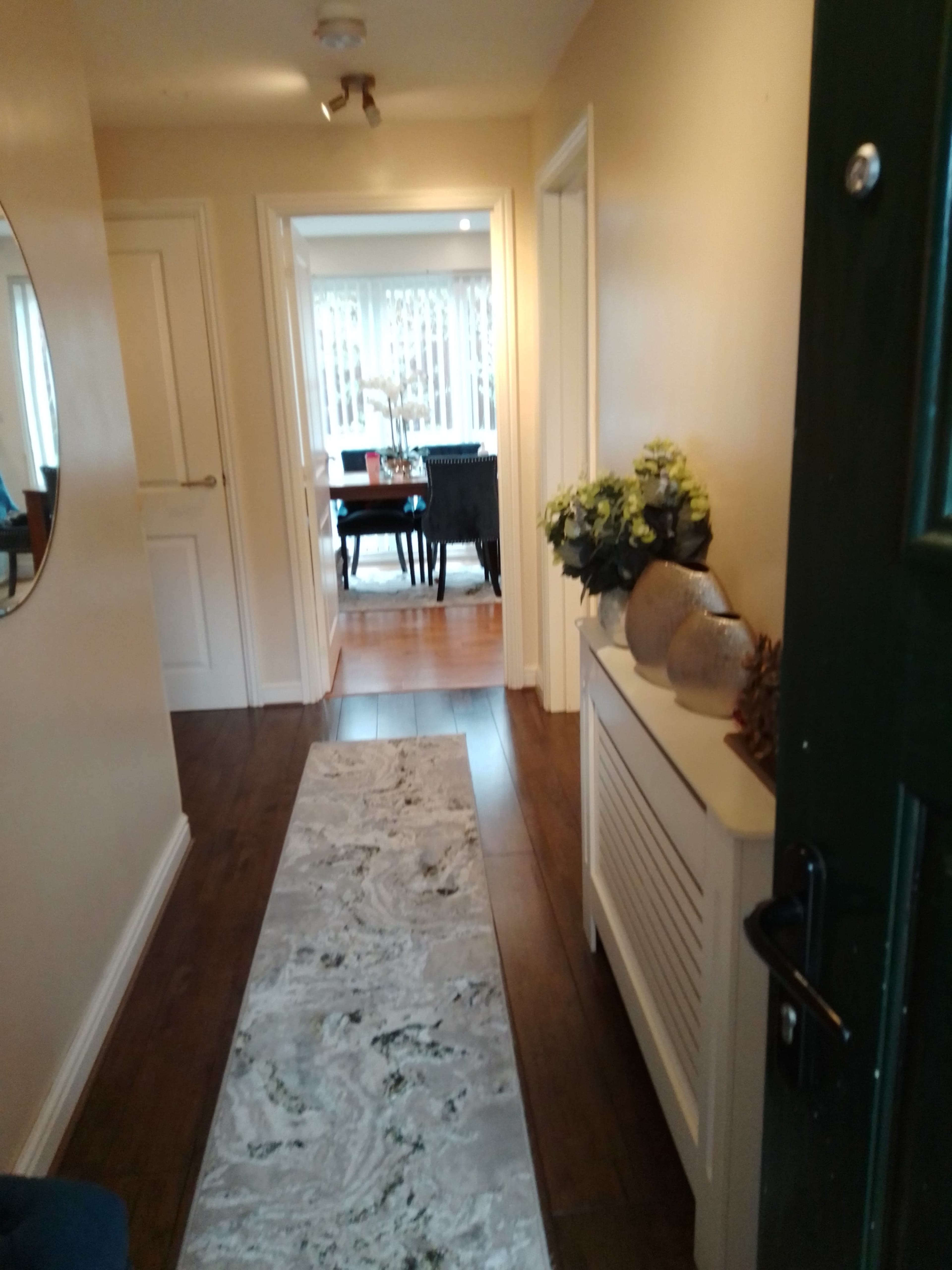 A hallway with a decorative rug, leading to a dining area in the background, flanked by doors on either side.