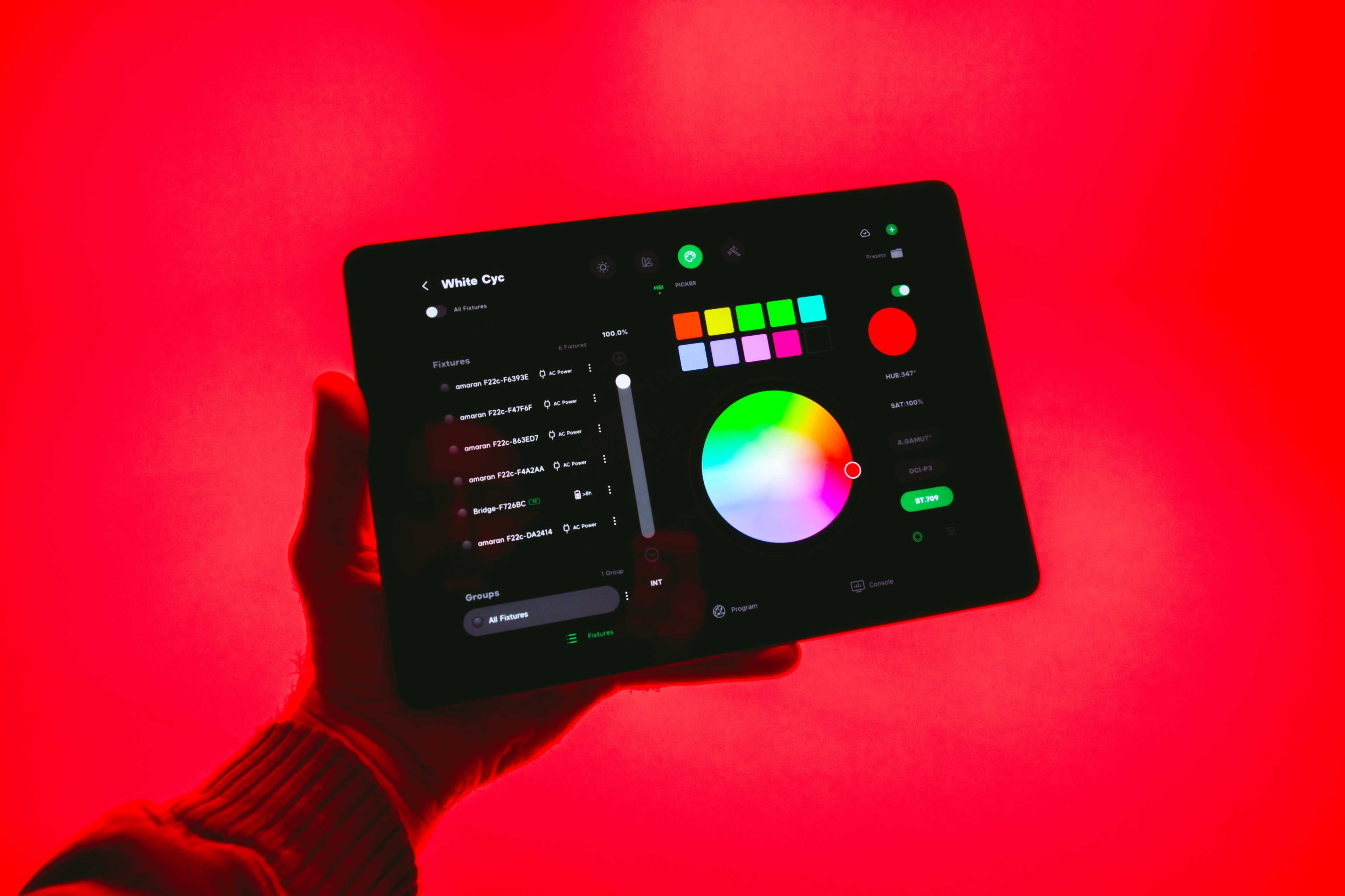 A hand holds a tablet displaying a color selection interface against a red background.