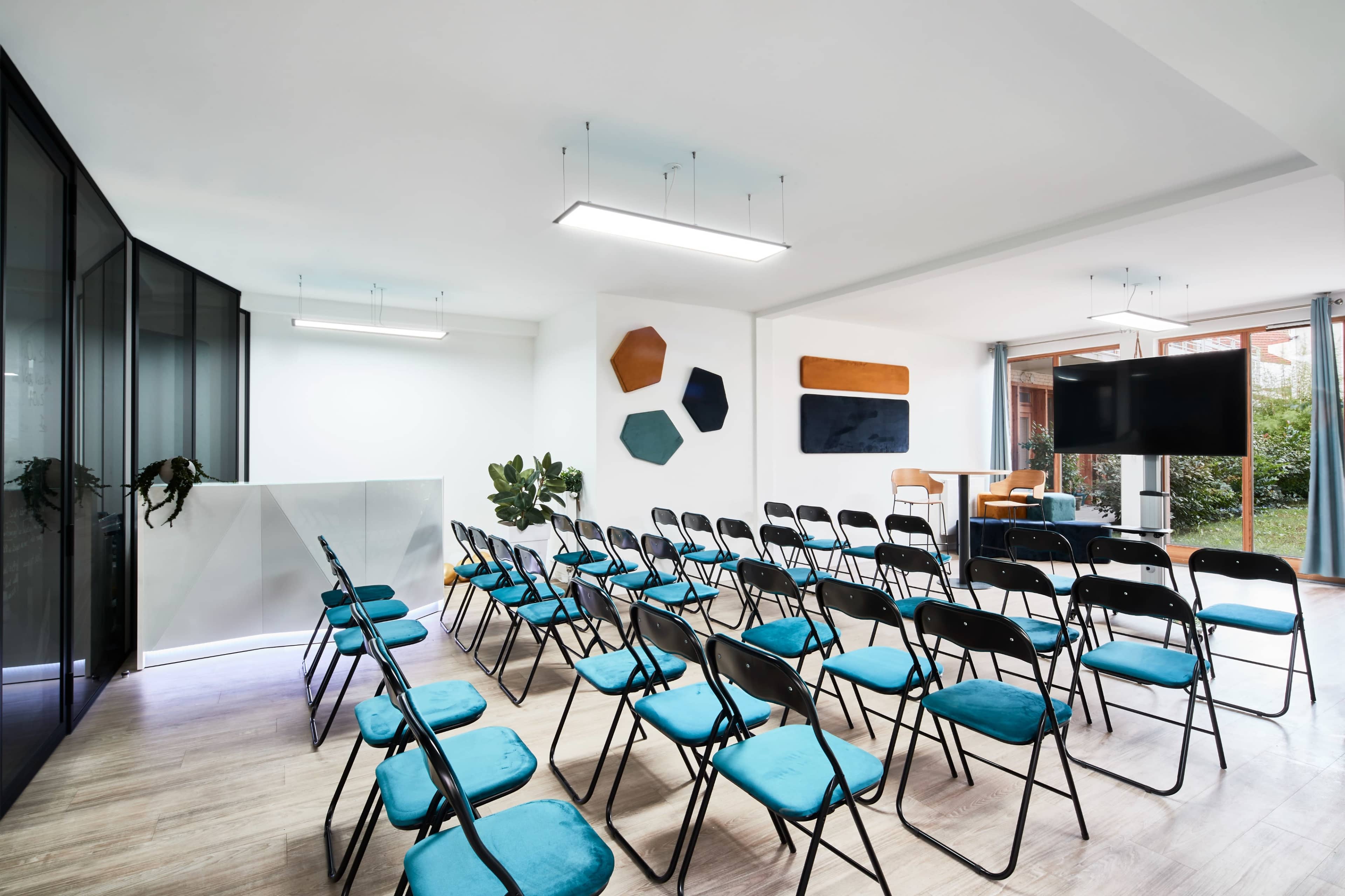 A meeting room is set up with rows of black chairs featuring teal cushions, along with a large screen and various wall decorations.