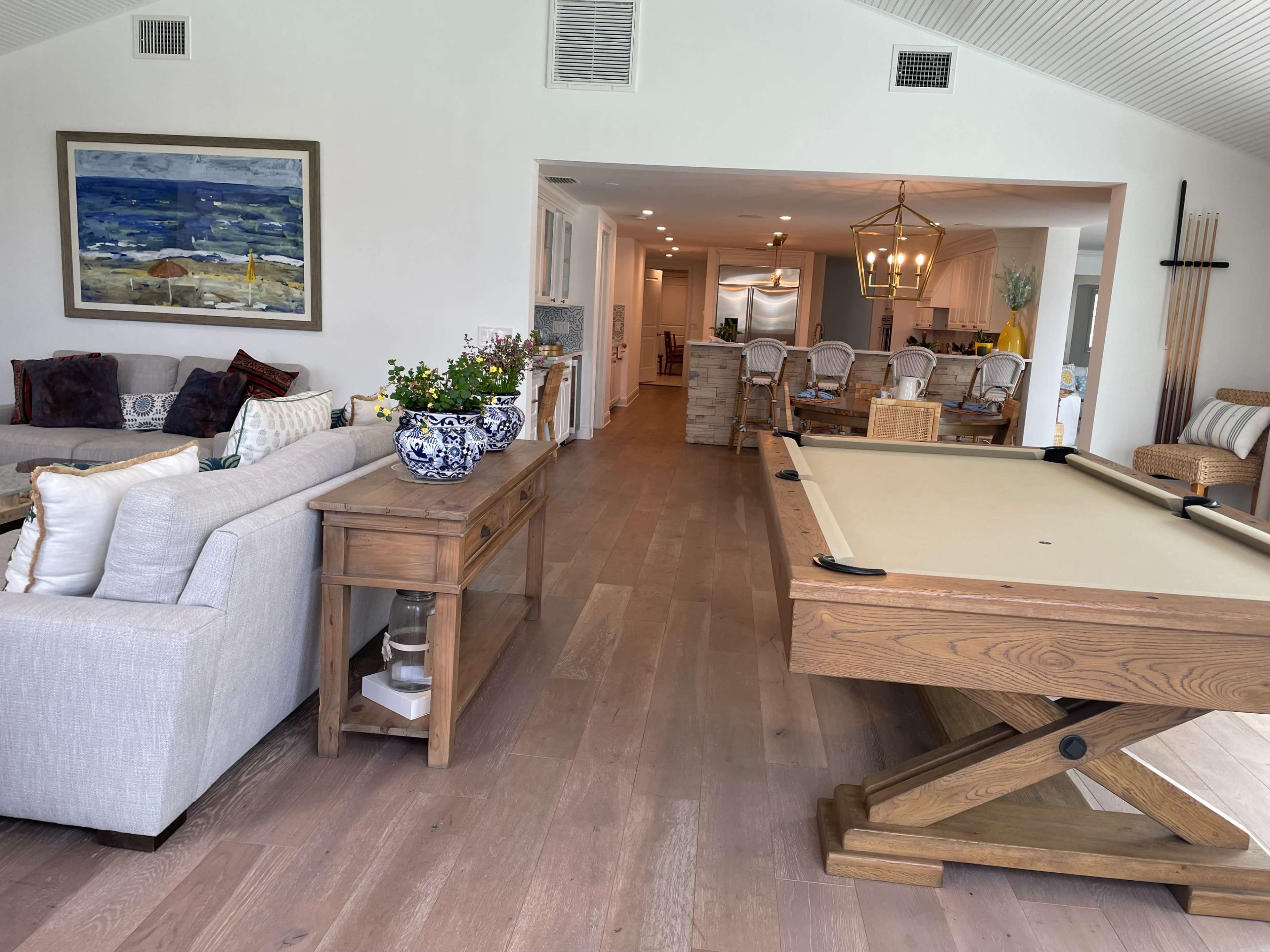 A spacious living area with a pool table, a console table with decorative items, and a view into a dining area with a large table and chairs.