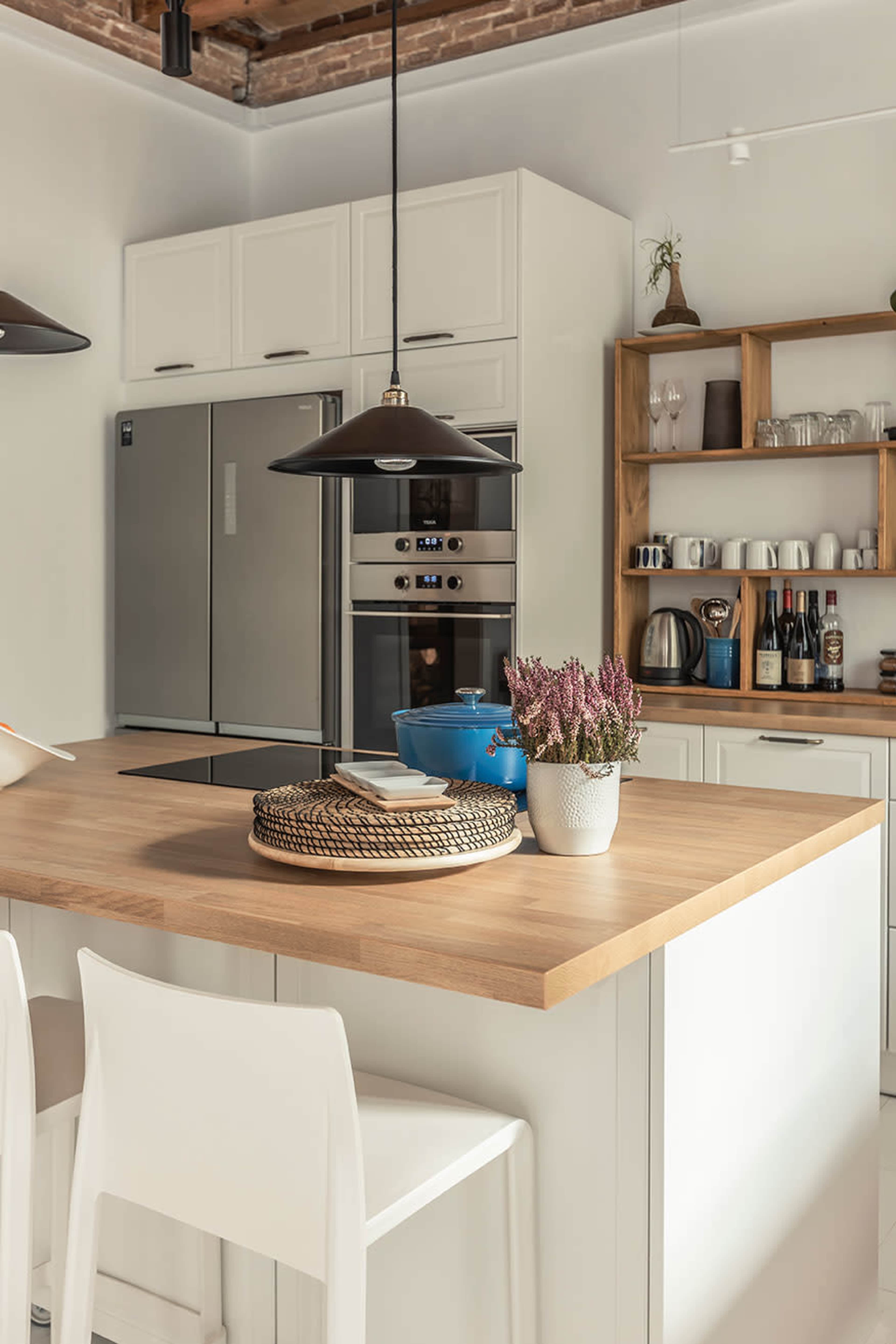 A modern kitchen features a wooden island with a basket and a potted plant, surrounded by appliances and neatly organized shelves.