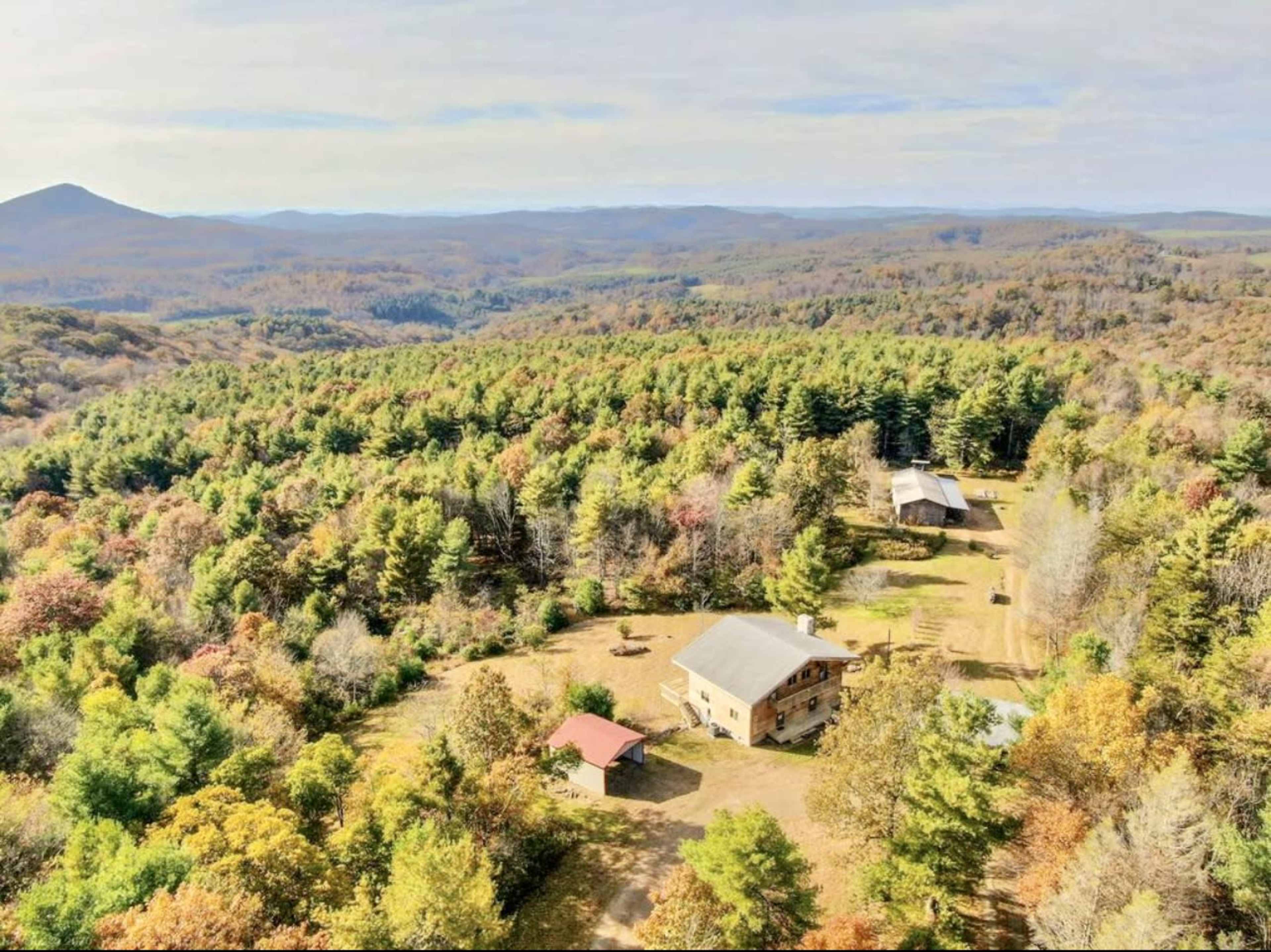 An aerial view shows a spacious property surrounded by colorful autumn foliage and mountains in the background.