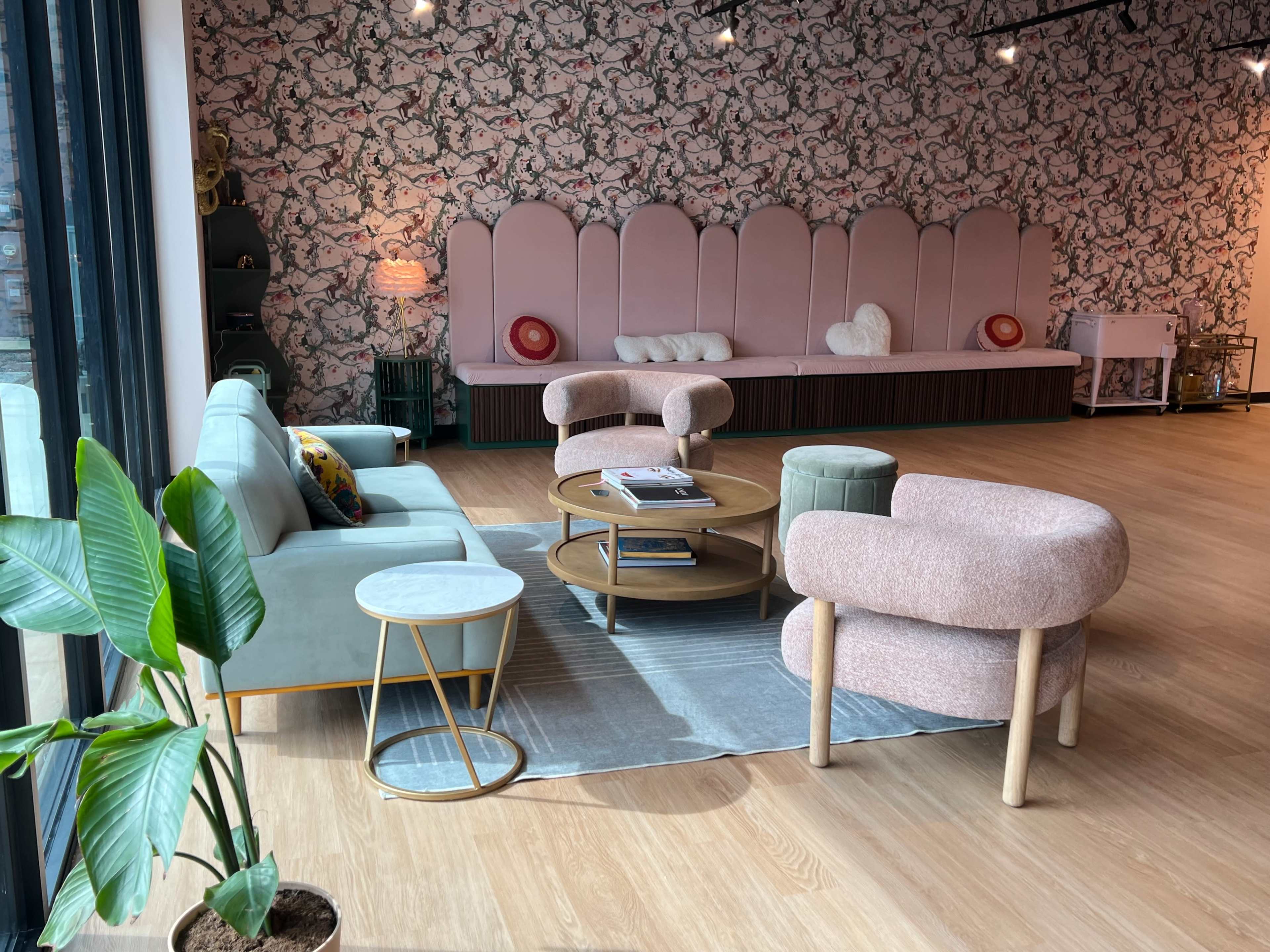 The scene depicts a modern lounge area with soft seating, a round coffee table, and a floral-patterned accent wall.