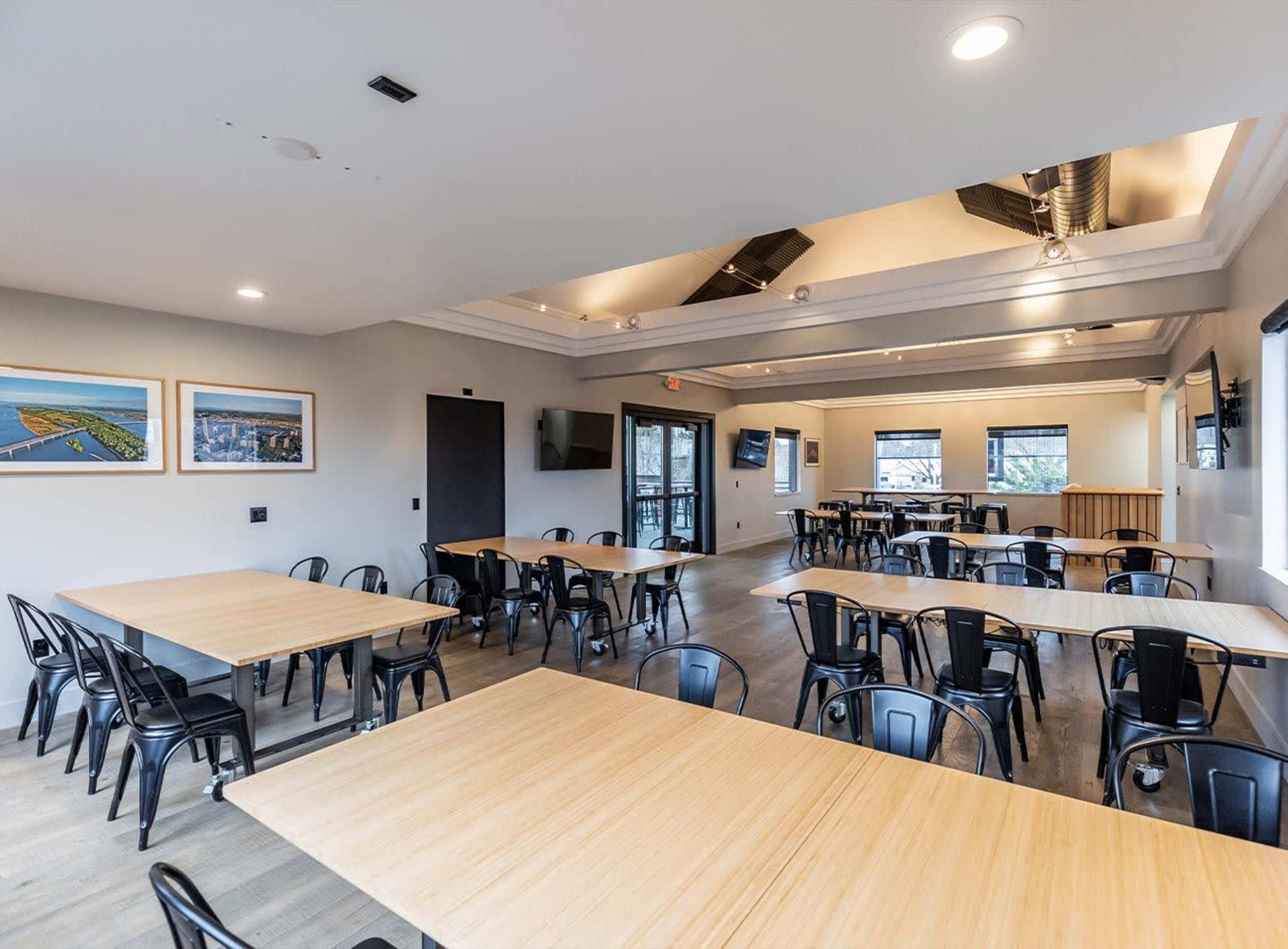 A large meeting room features multiple tables arranged in a spacious layout with modern decor and windows providing natural light.