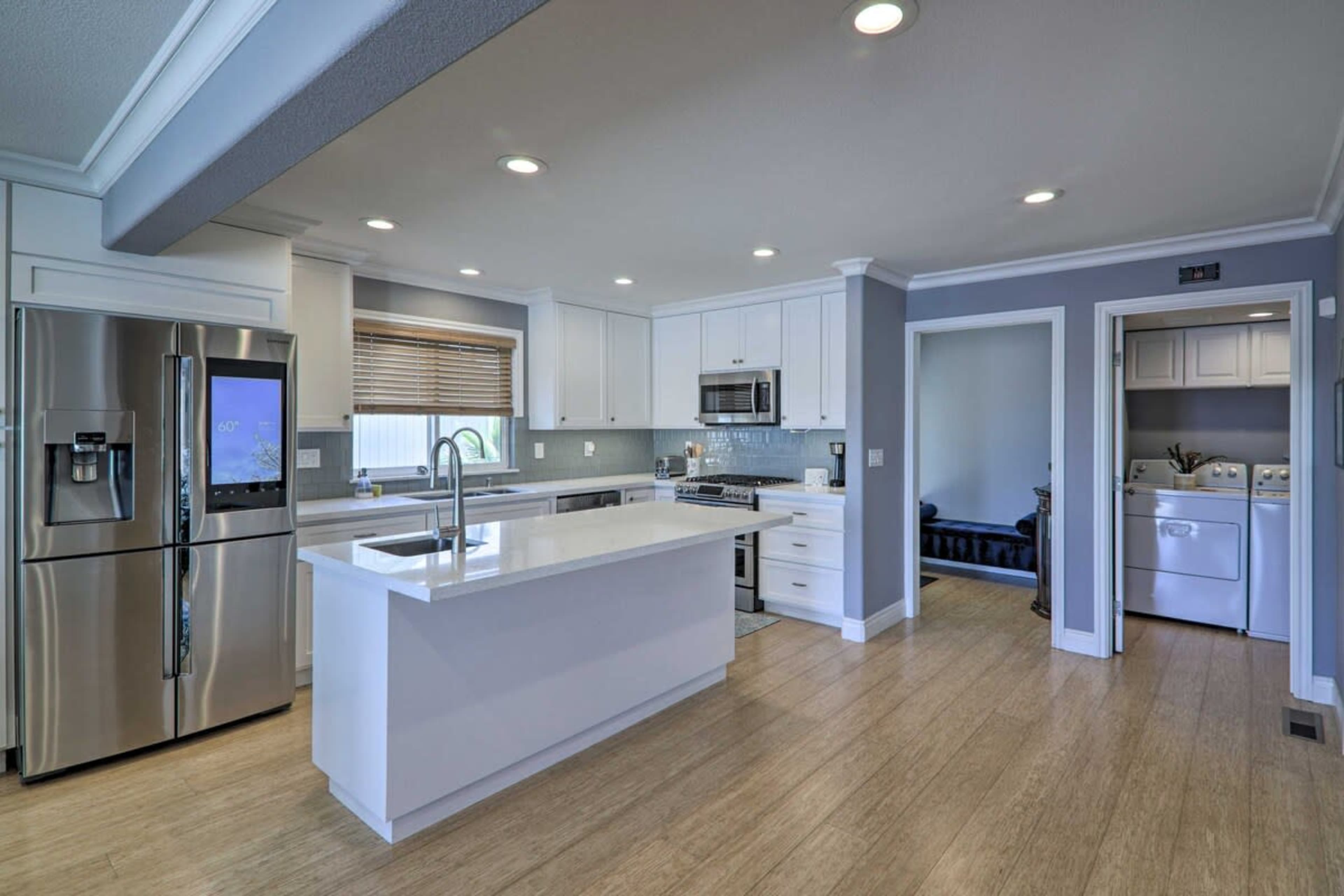 A modern kitchen with white cabinets, stainless steel appliances, and a spacious island, leading to a laundry area in the background.