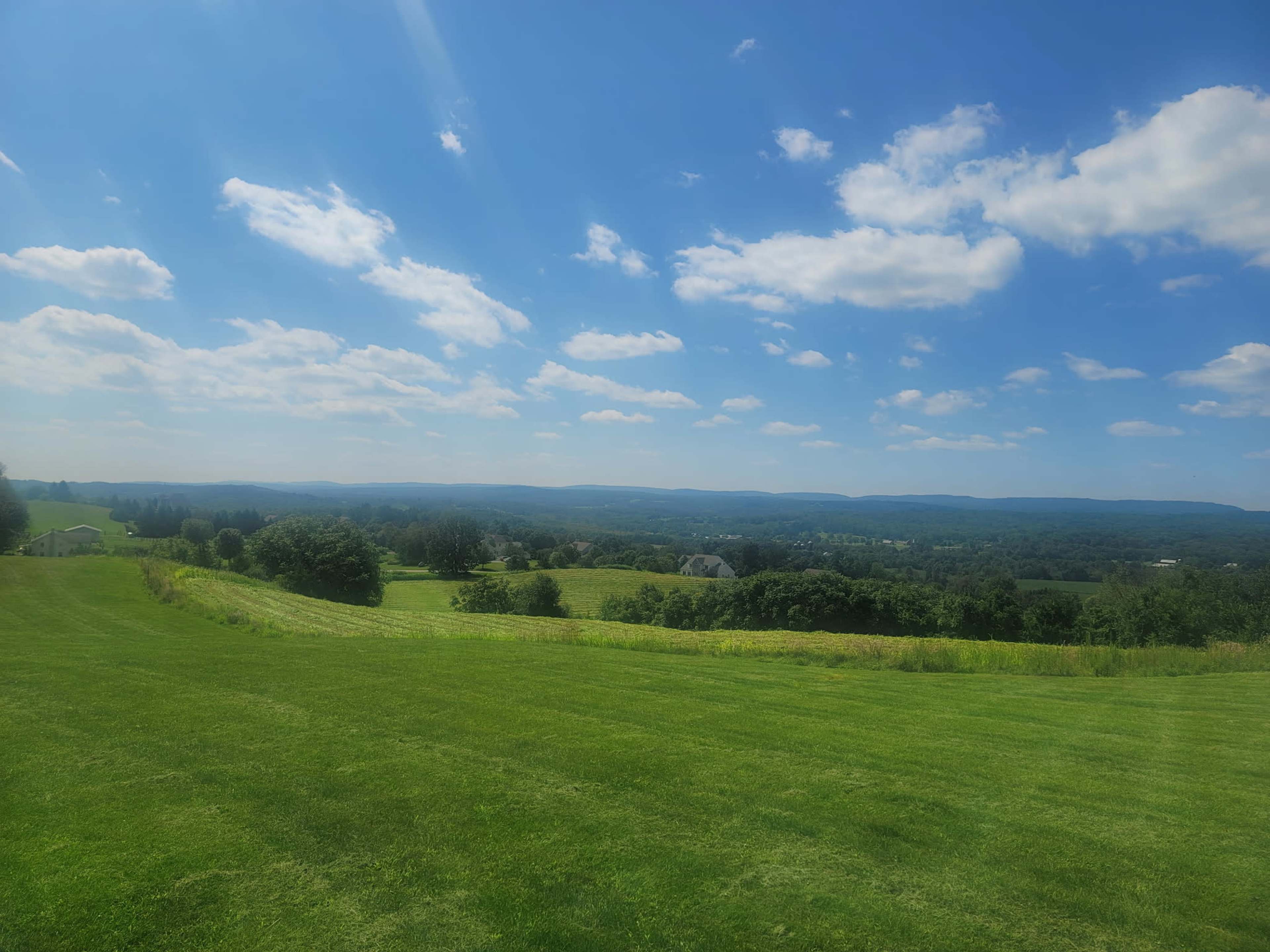 The image shows a vast green landscape with rolling hills under a blue sky featuring scattered clouds.
