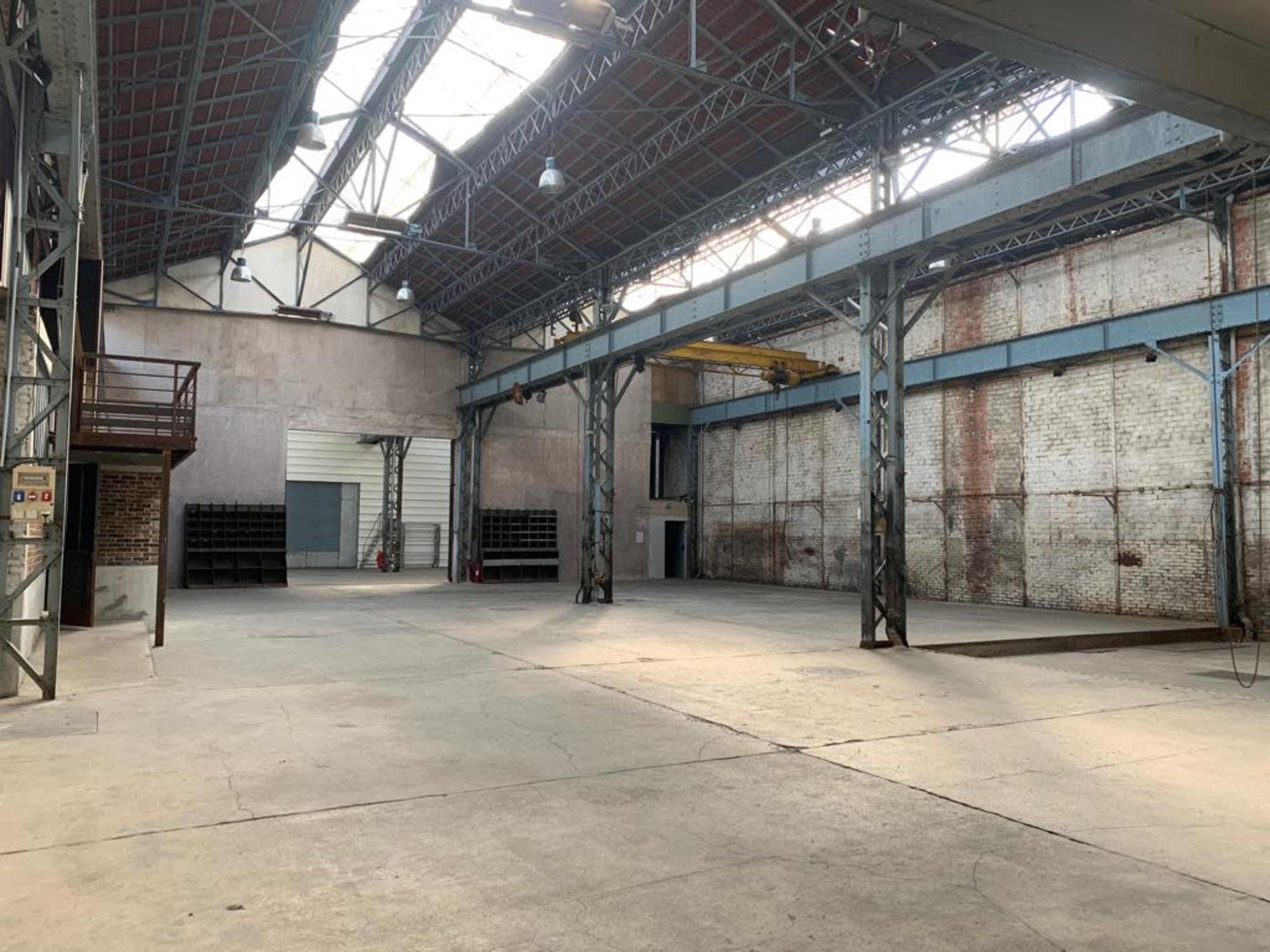 An empty industrial warehouse features high ceilings, exposed beams, and concrete floors.