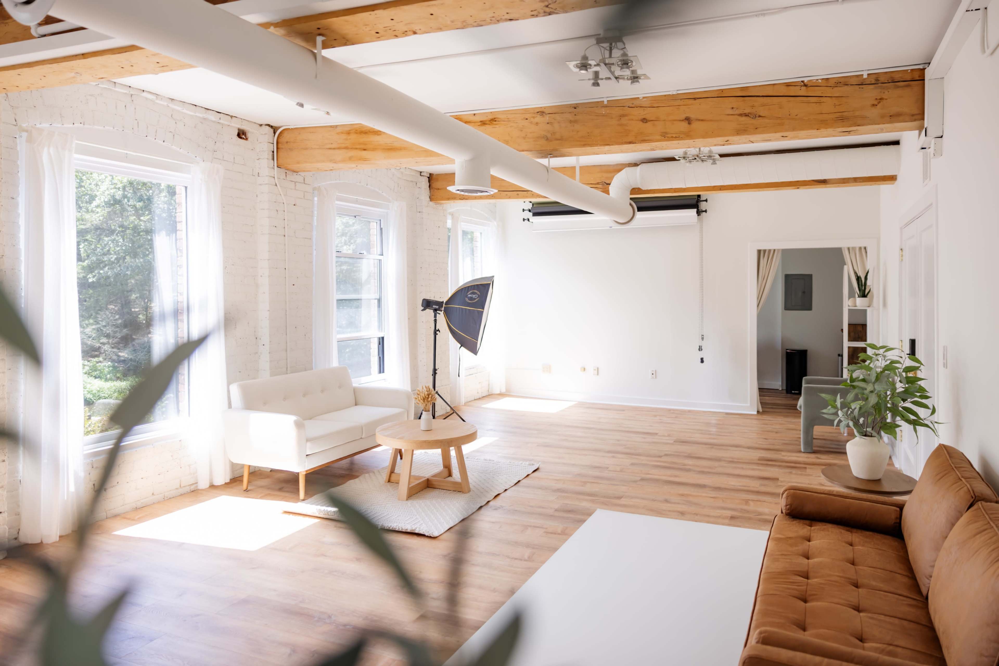 A spacious, well-lit room features a white brick wall, wooden beams, and minimalistic furniture, including two sofas and a coffee table.