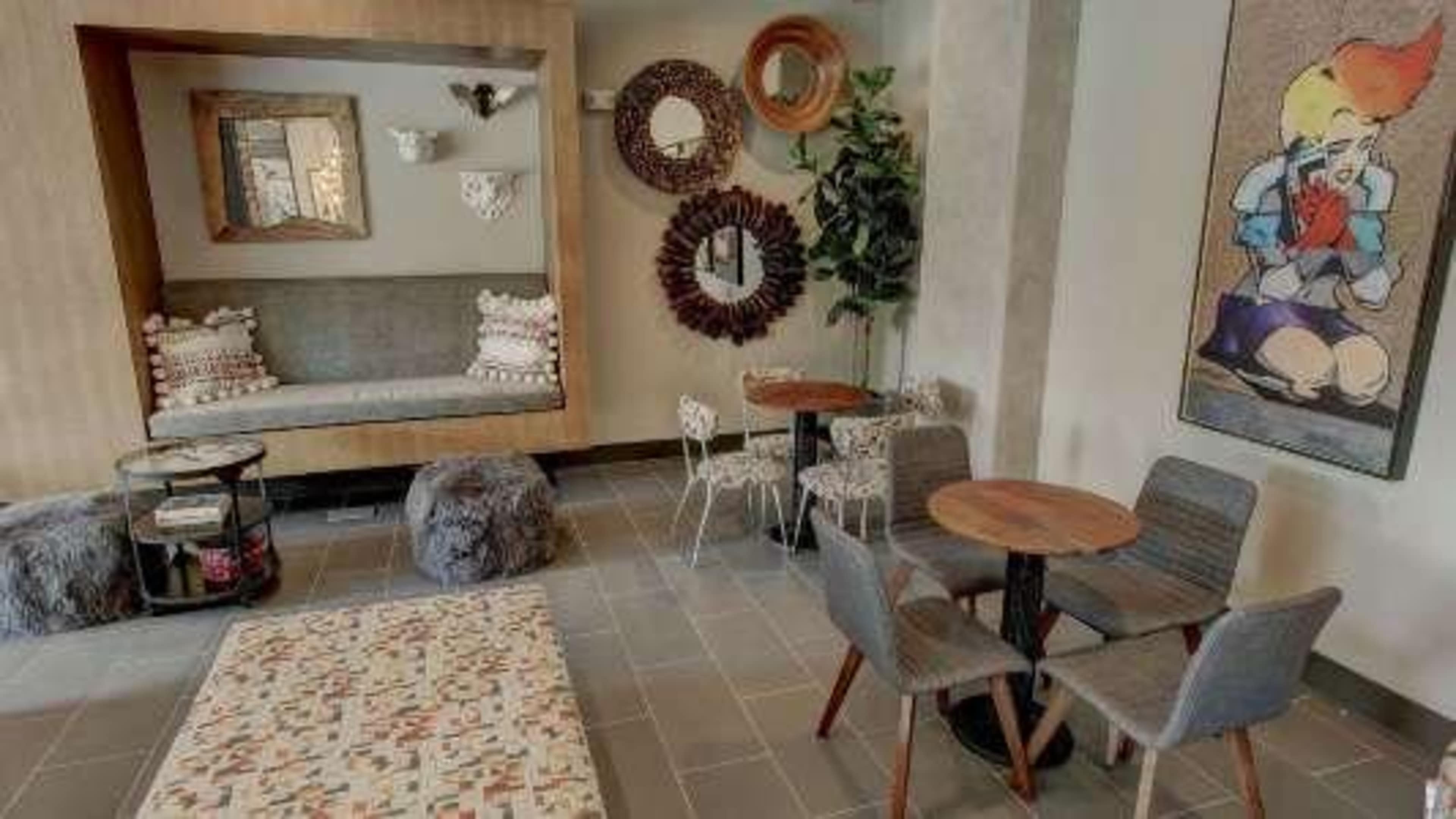 The image shows a cozy café area featuring a small seating nook, circular mirrors on the wall, and several tables and chairs arranged on a tiled floor.