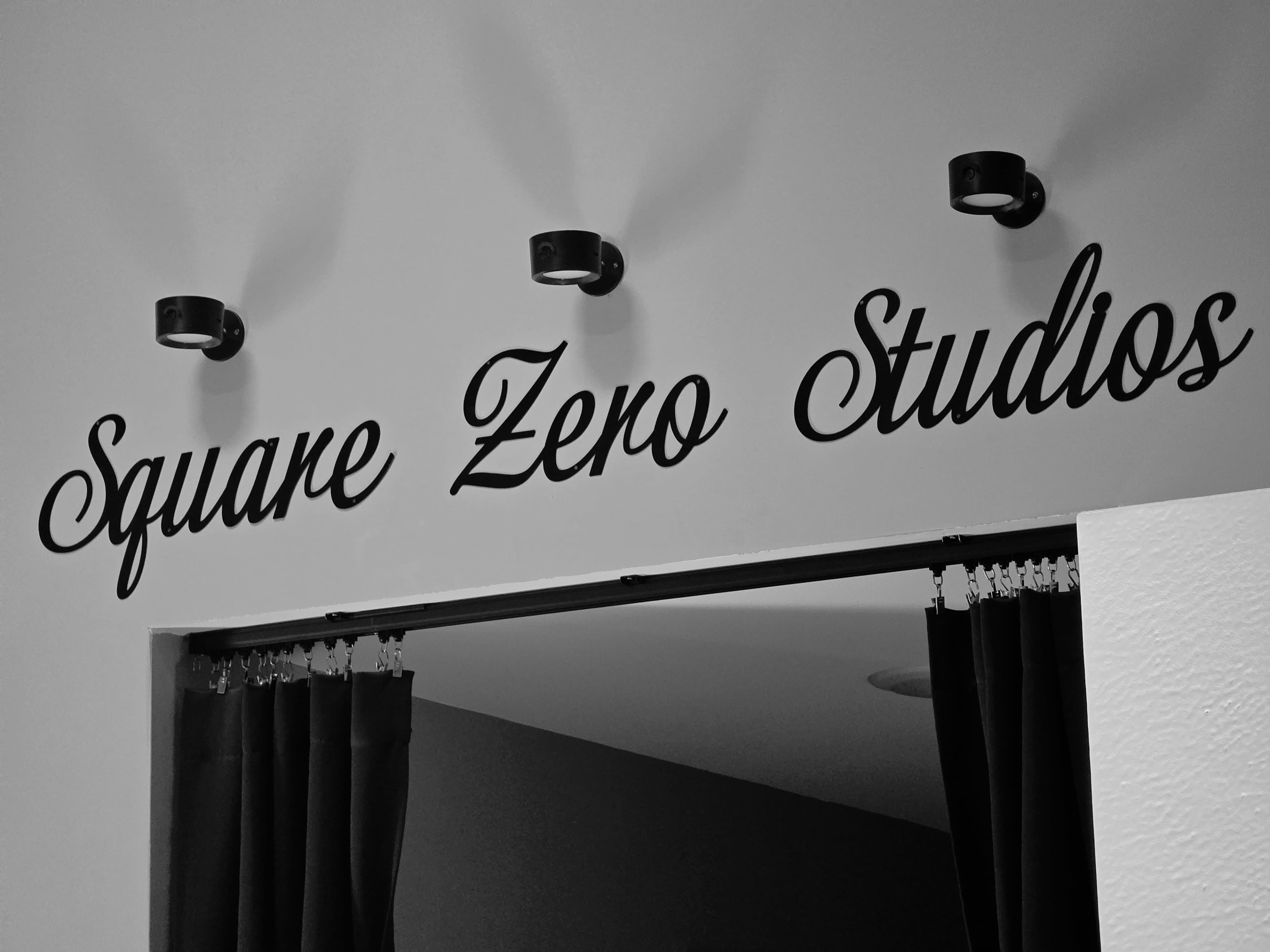 The image features the text "Square Zero Studios" displayed in a decorative font on a wall above an entrance with dark curtains.
