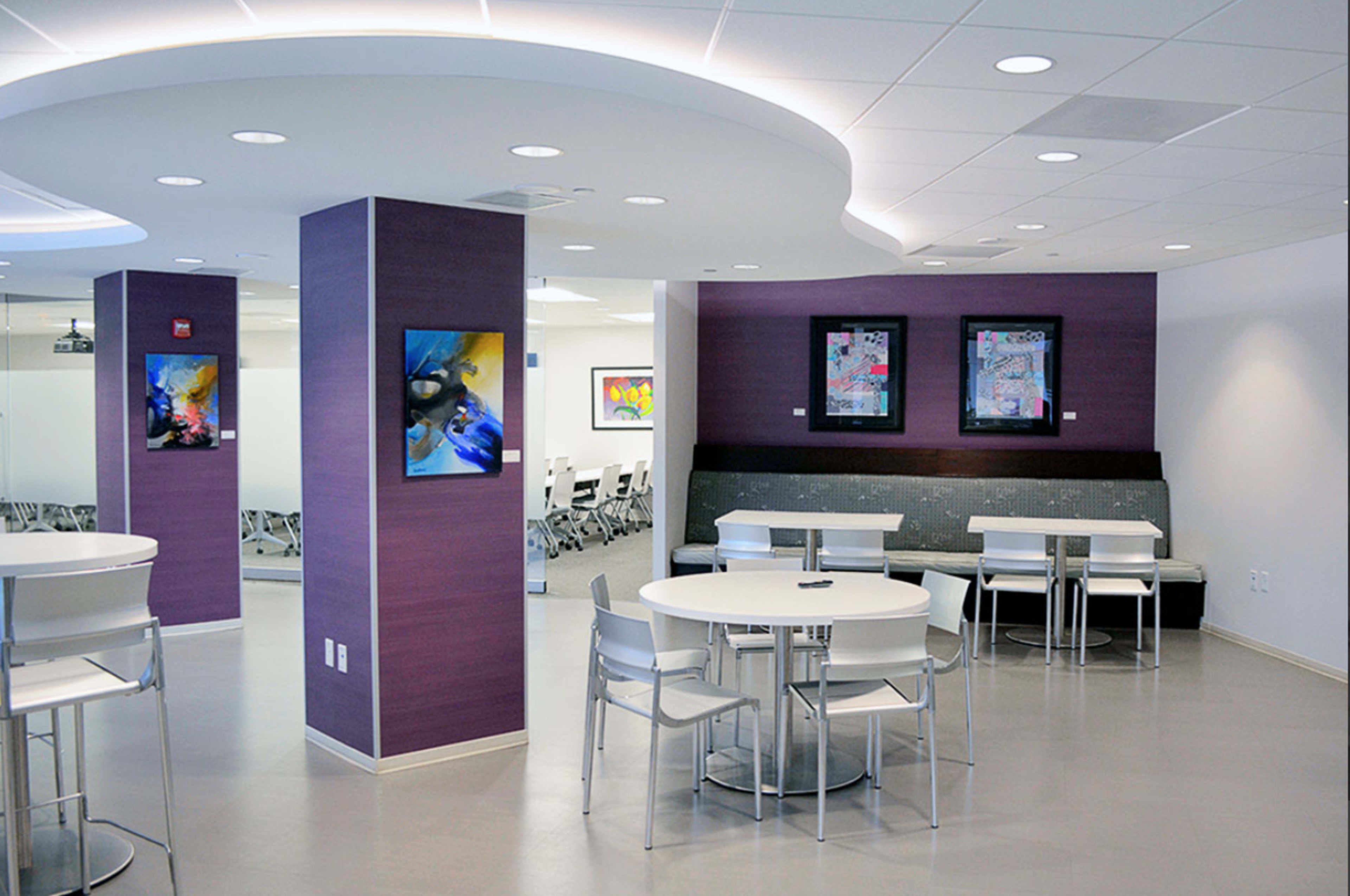 The image shows a modern interior design of a café-like space with circular tables and chairs, purple accent walls, and colorful artwork displayed.