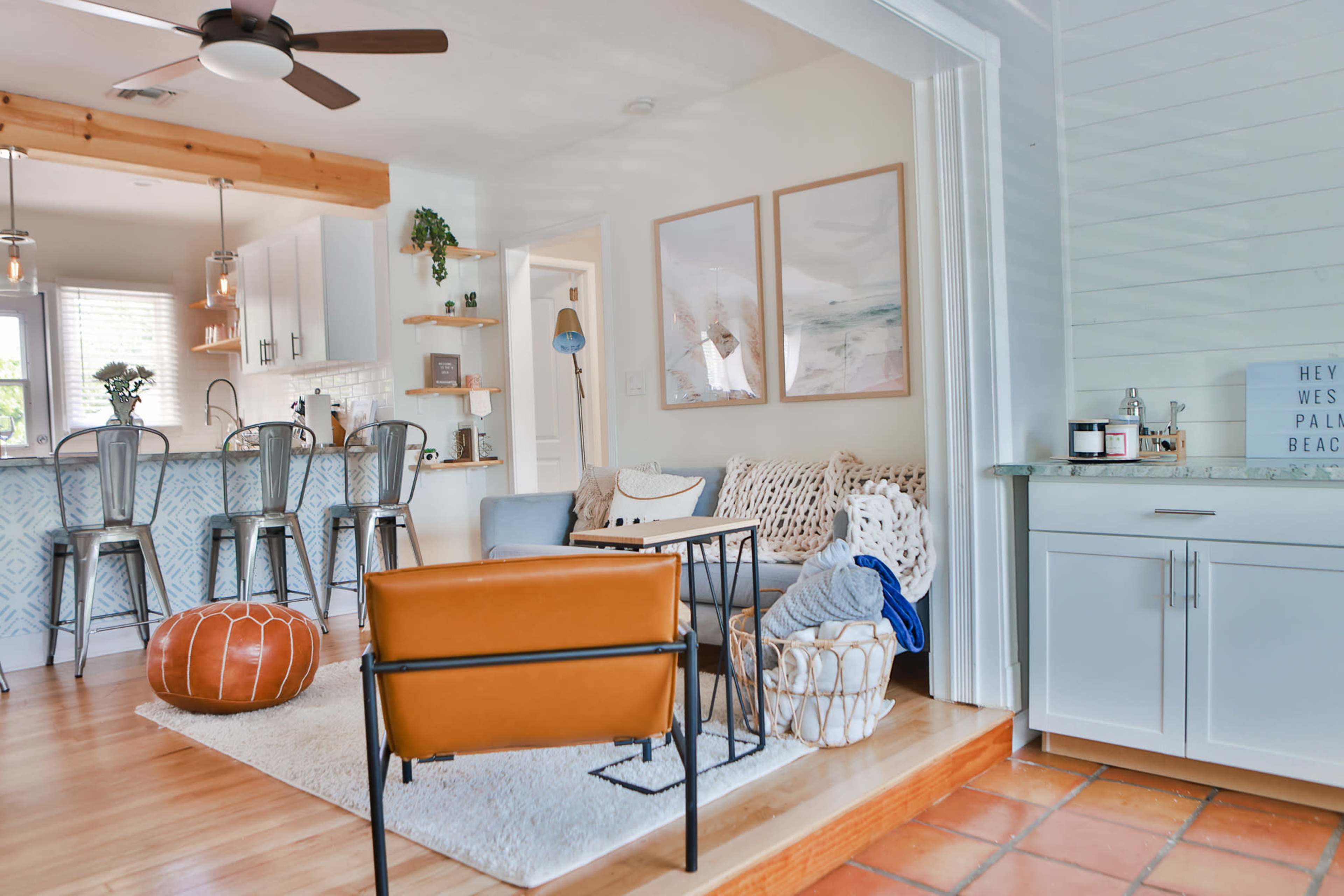 A cozy living space features a beige sofa, colorful decor, and a kitchen bar with stools in the background.