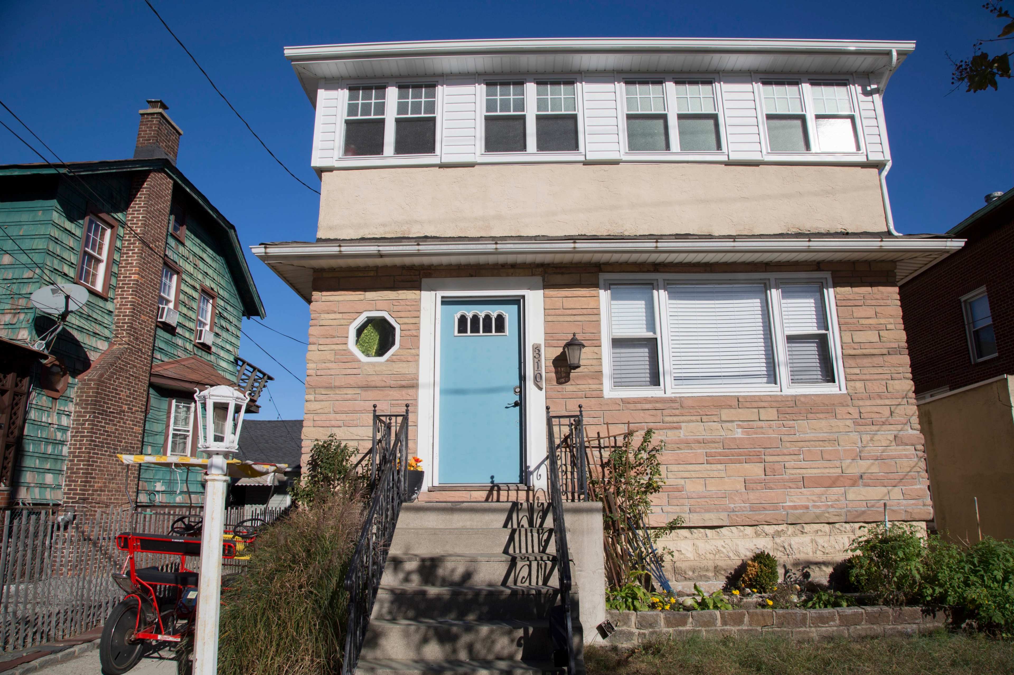 A two-story residential building with a light blue door and a rounded window, flanked by neighboring homes.