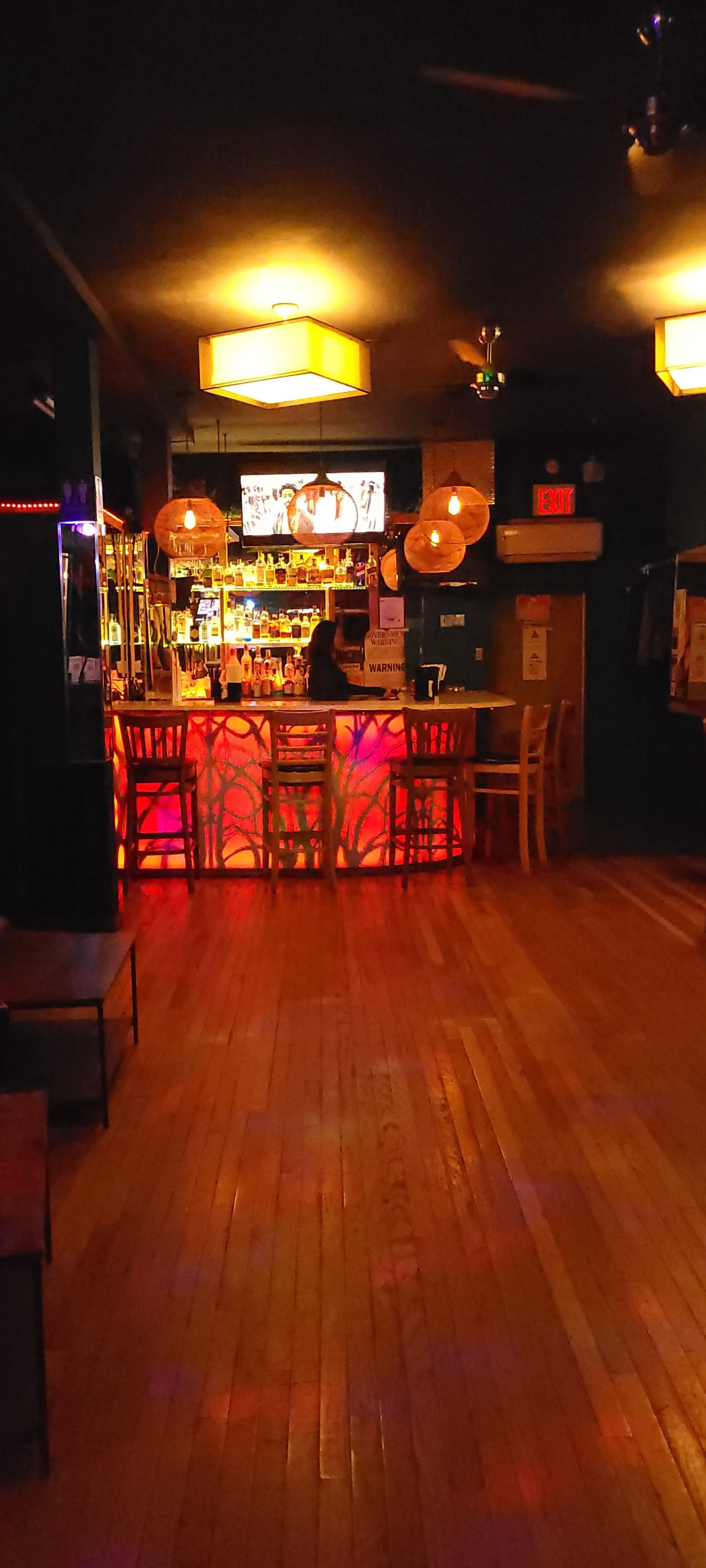 A dimly-lit bar features a brightly illuminated backlit counter, with hanging lamps casting warm light over the empty seating area.