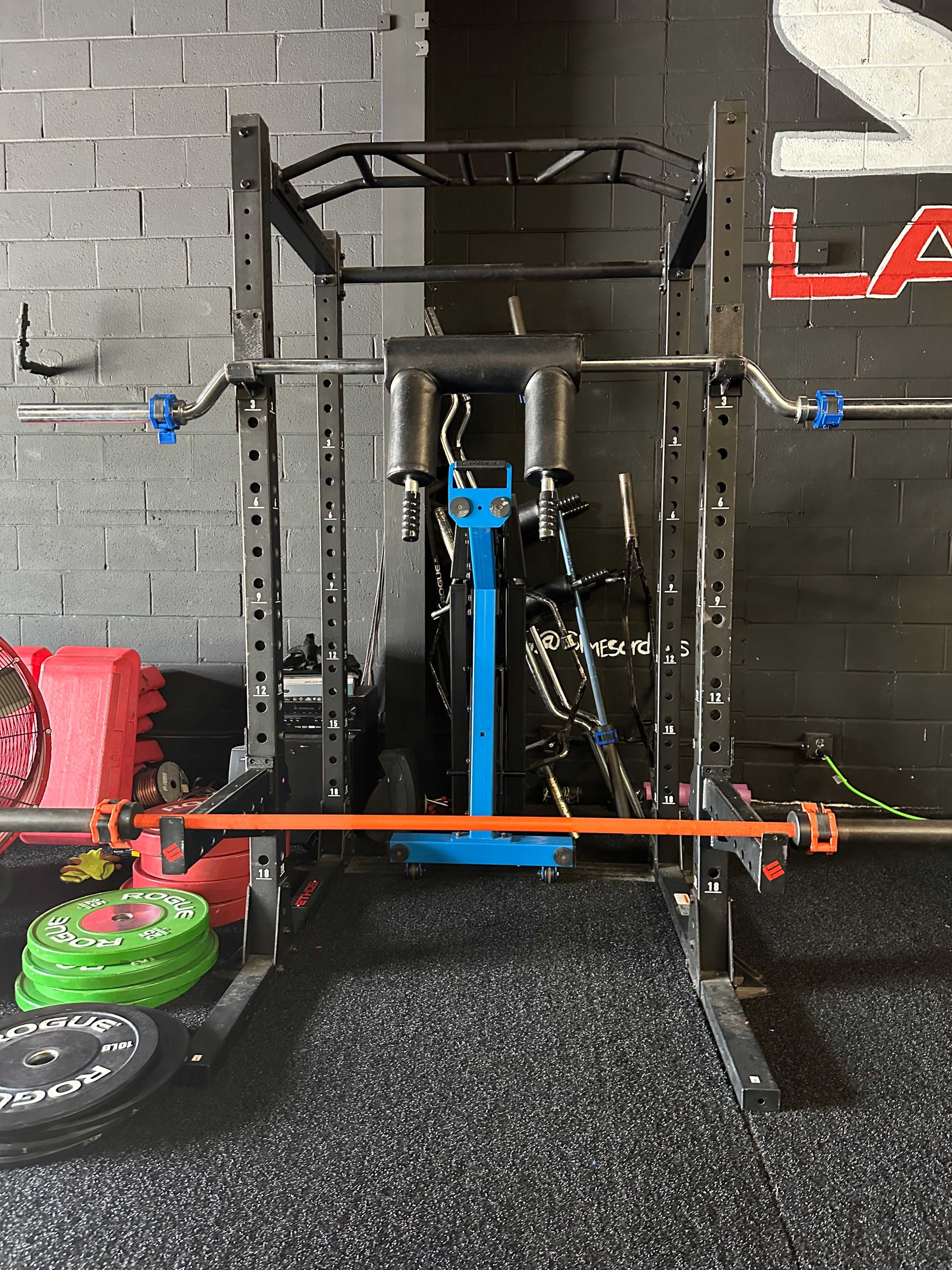 A power rack with a barbell set on it, surrounded by weight plates and gym equipment in a fitness facility.