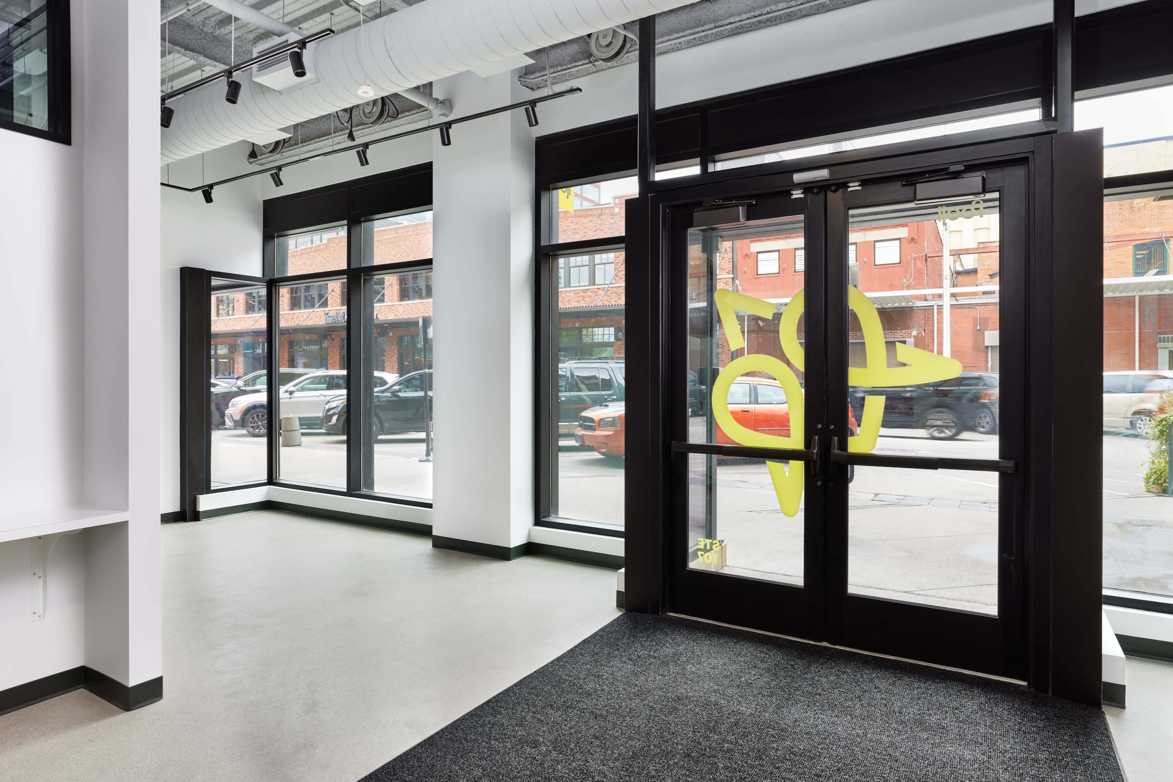 The interior of a modern lobby with large glass doors and windows, featuring a prominent yellow design element.