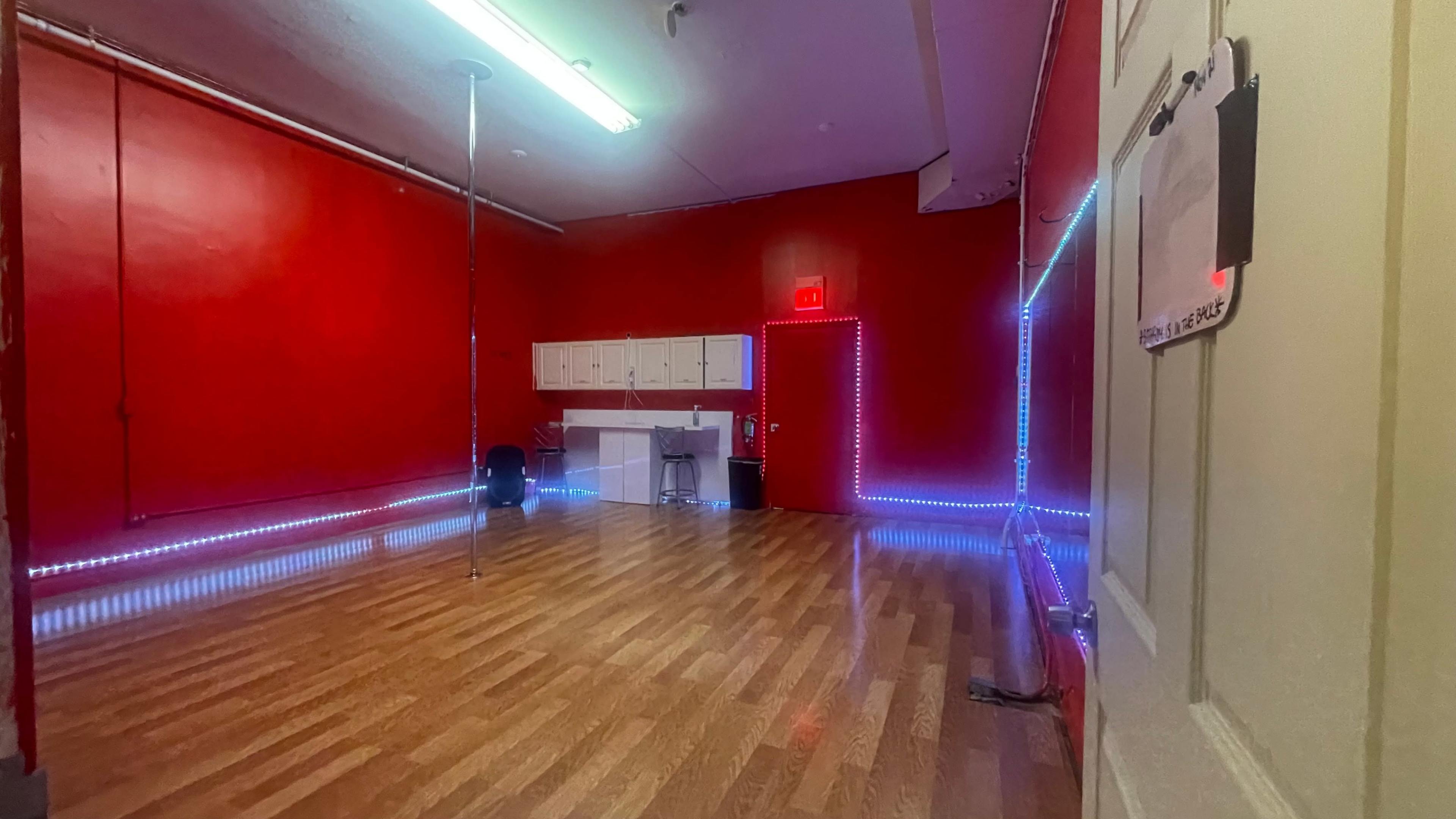 A room with red walls, wooden flooring, a pole in the corner, and illuminated edges along the walls.