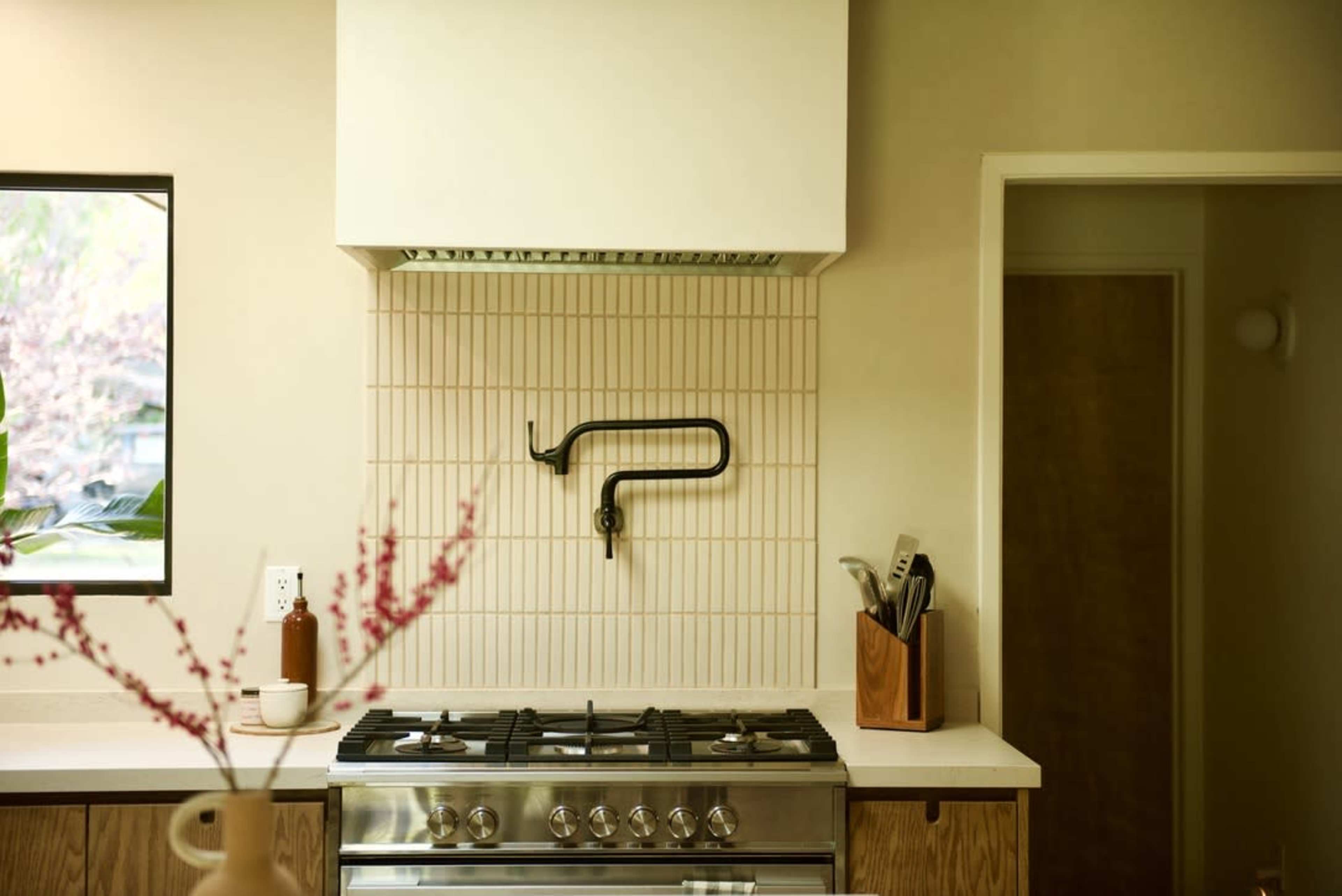 A modern kitchen features a stainless steel stove, a wall-mounted hood, and a tiled backsplash with a black faucet.