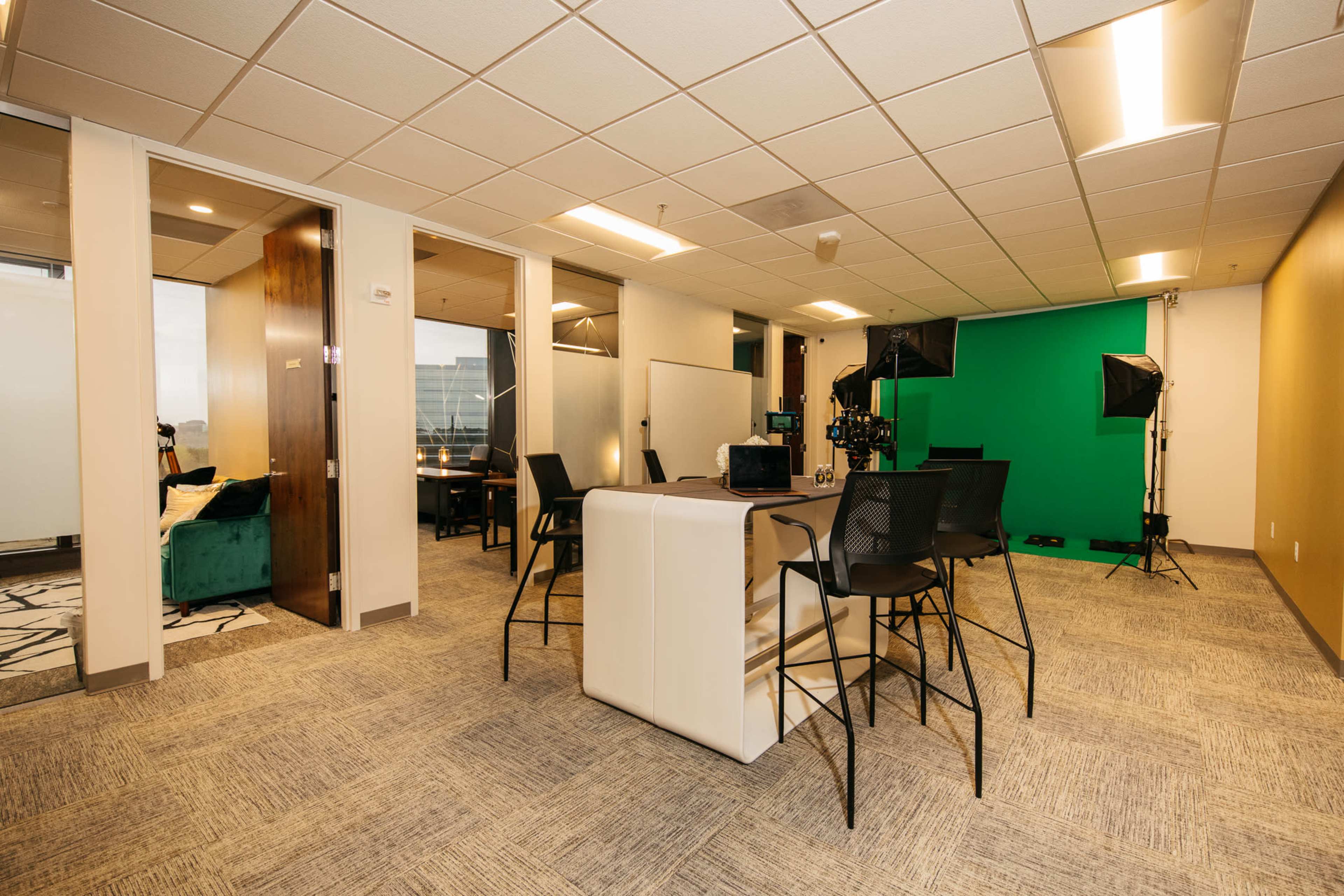 A modern workspace with a green screen setup, several cameras, a large table for meetings, and seating arrangements.