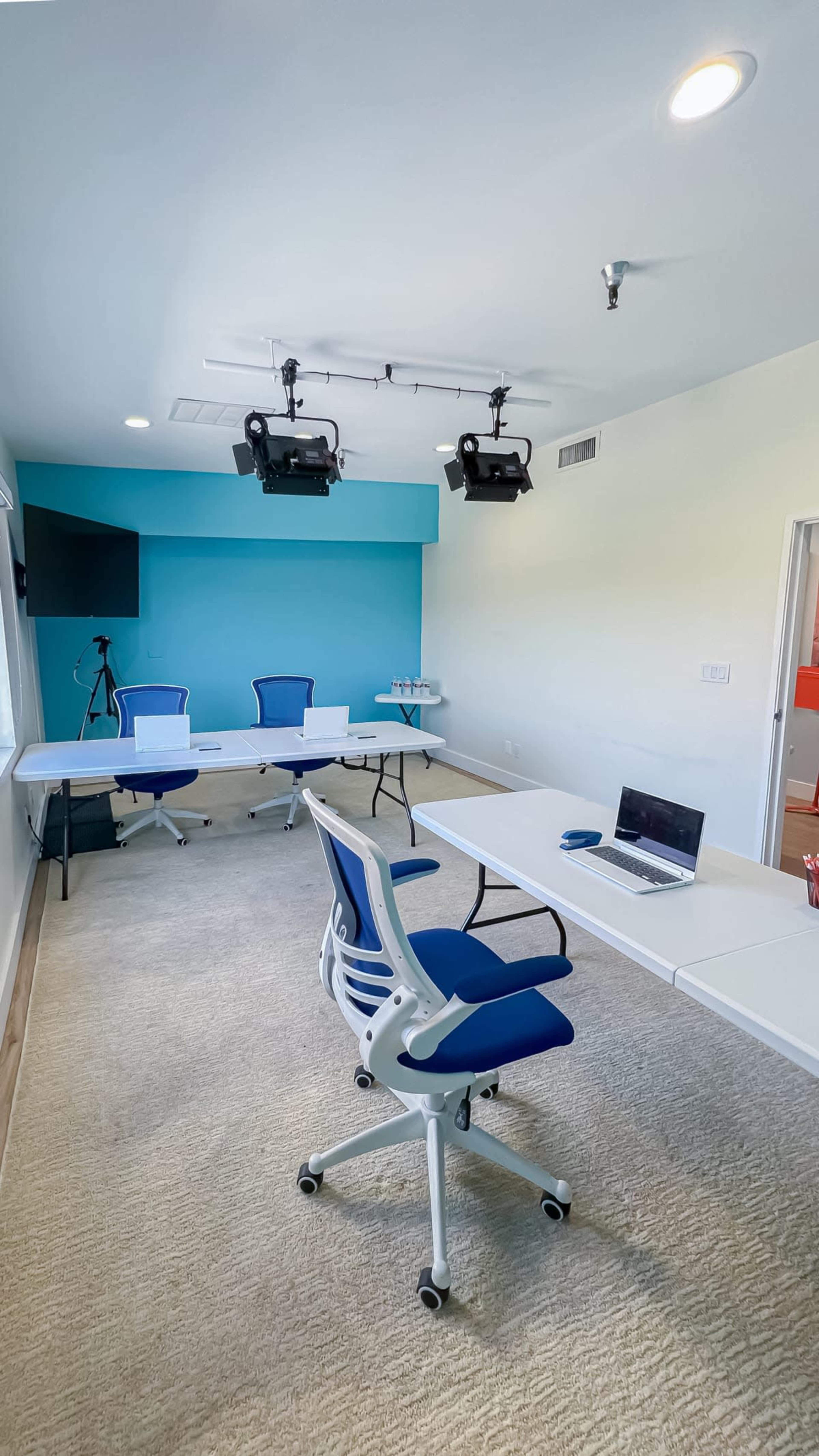 The image shows a modern, empty conference room with blue accent walls, two projectors mounted on the ceiling, and tables arranged for a meeting.