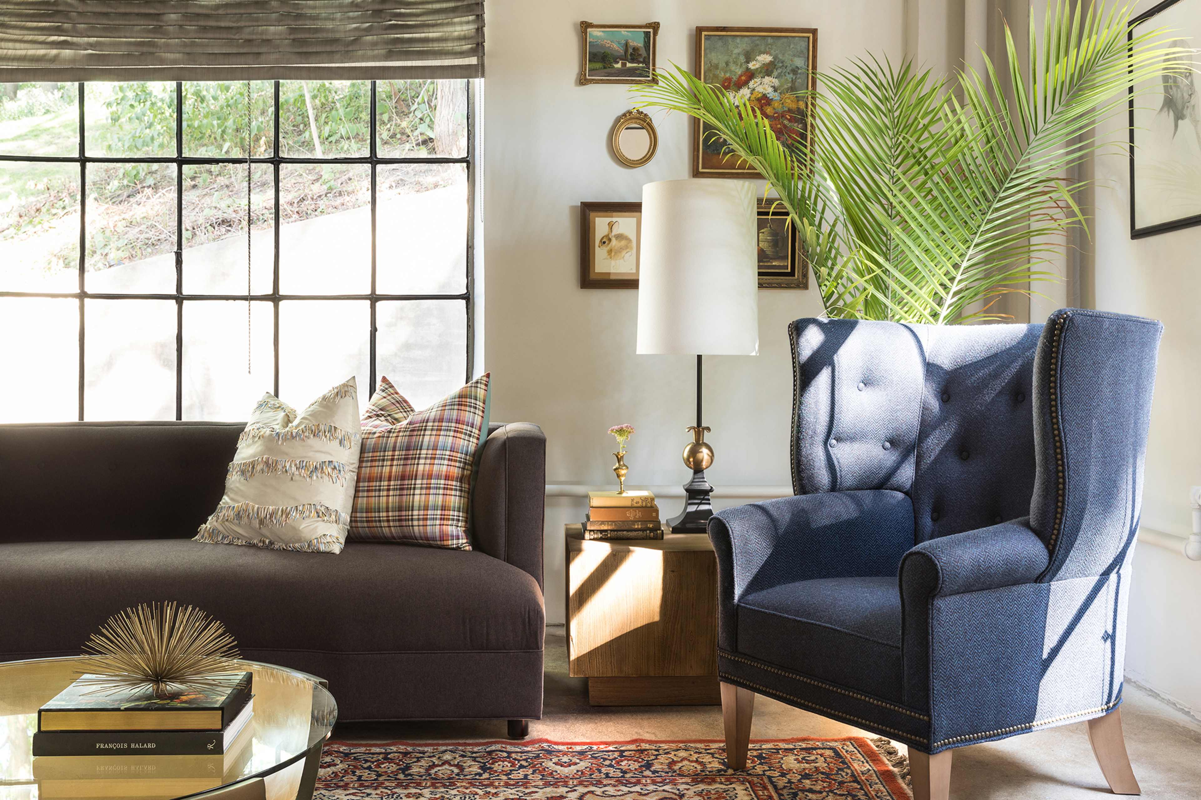 The scene shows a living room with a dark sofa, a blue armchair, a round coffee table, and a tall lamp beside a window with natural light.
