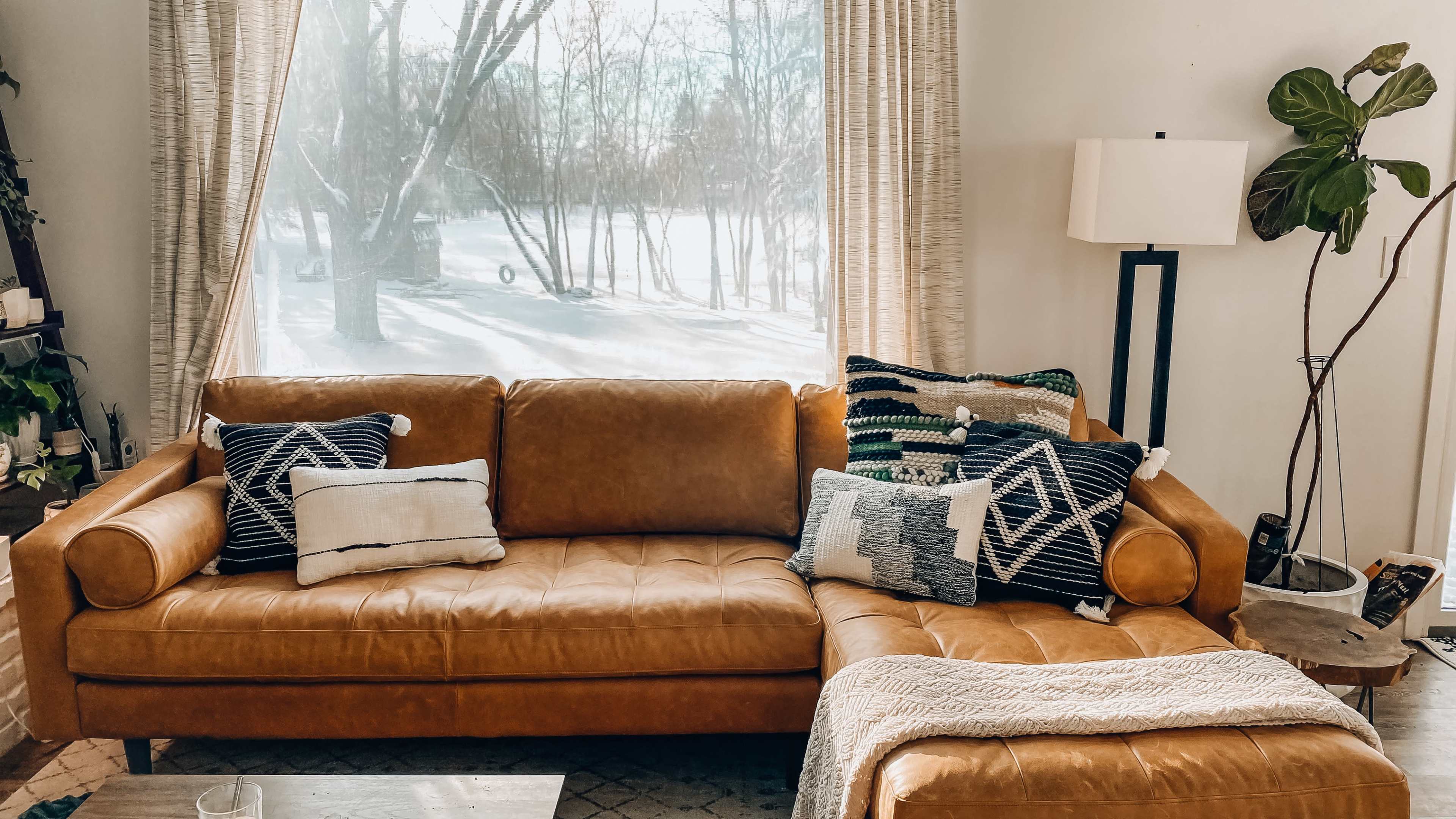 A brown leather sectional sofa adorned with patterned throw pillows, positioned by a window overlooking a snowy landscape.