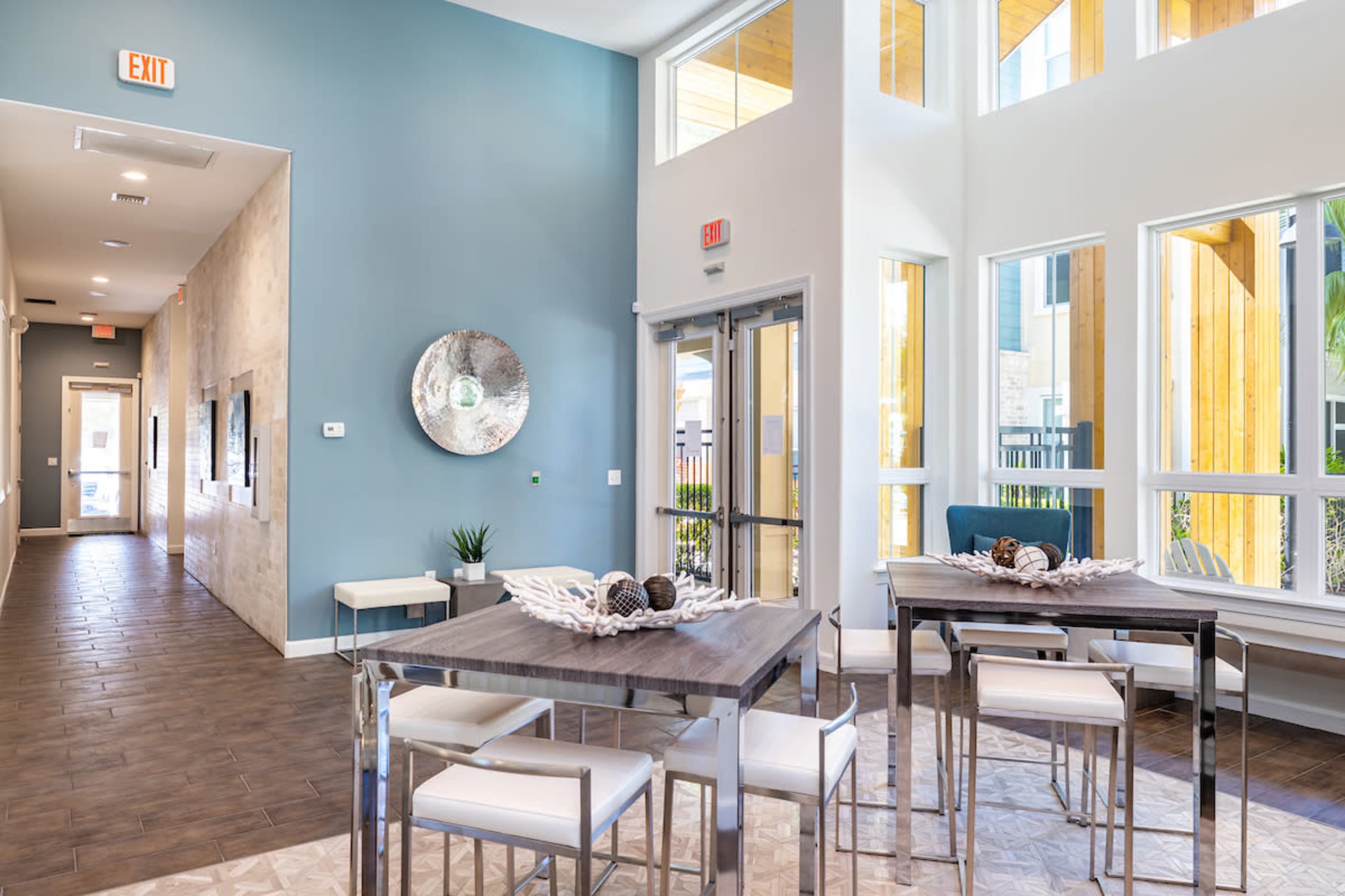 A modern lobby area with large windows, a seating arrangement with tables, and decorative elements, all featuring a blend of light and pastel colors.