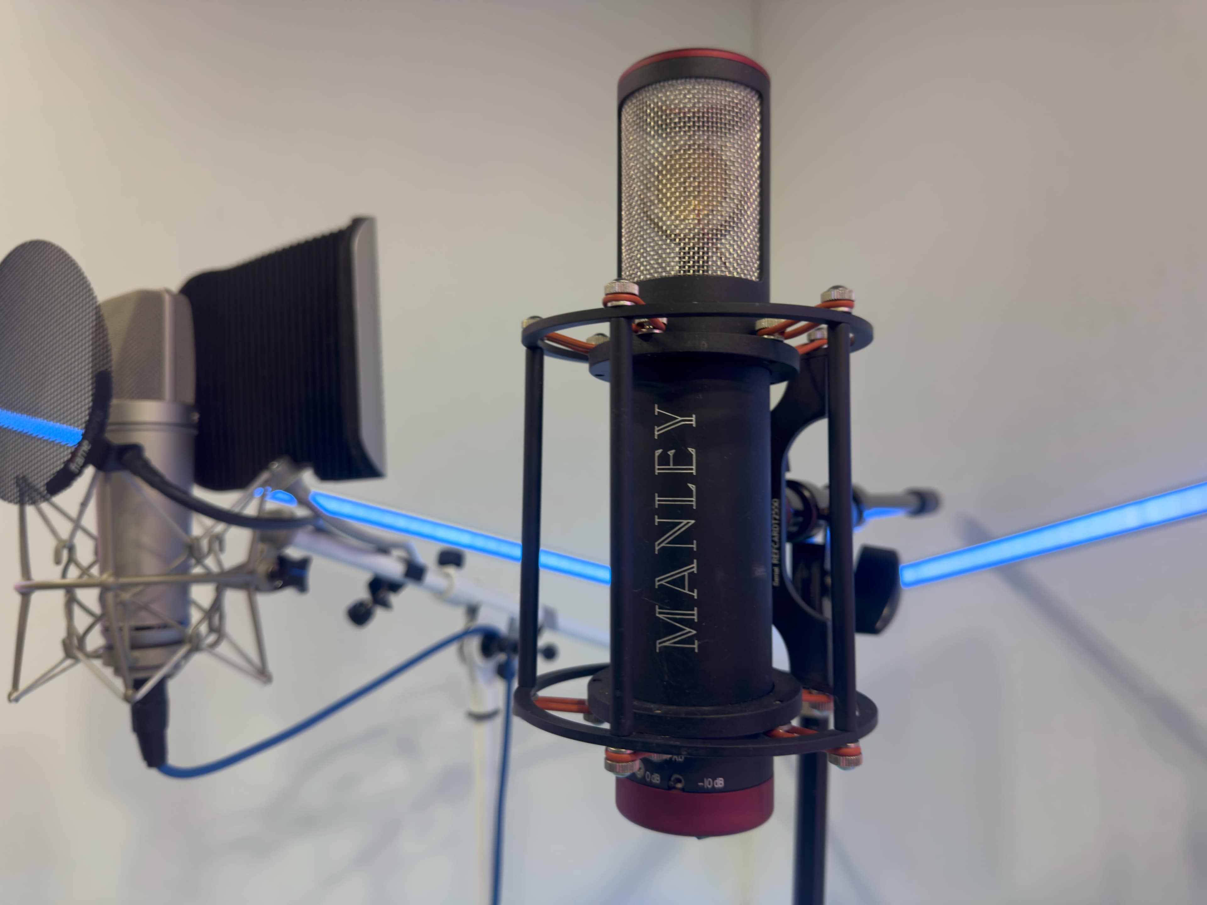 A black and silver microphone is mounted in a shock mount, with a blue-lit audio setup visible in the background.