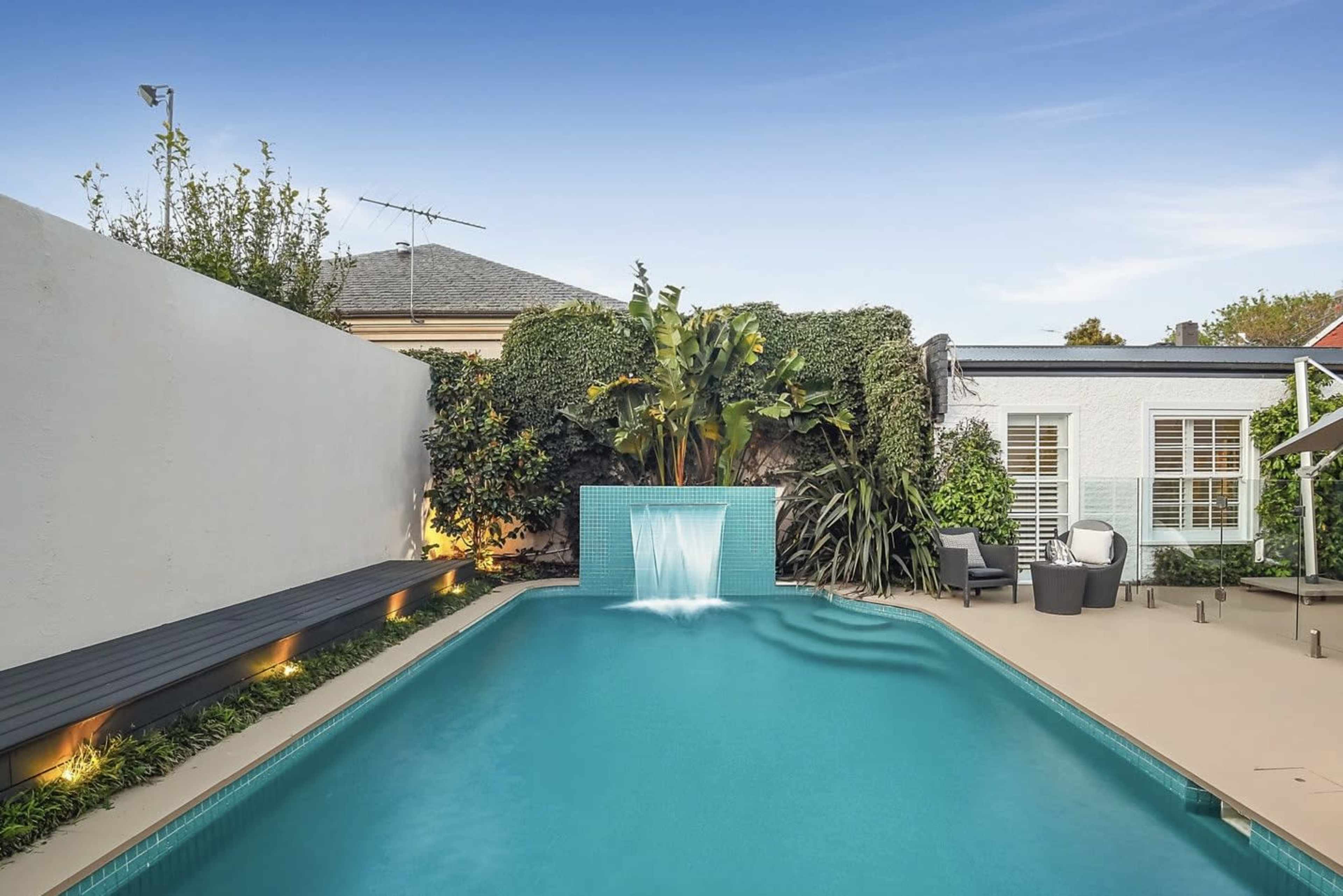 A swimming pool with a water feature surrounded by lush greenery and a modern patio area.