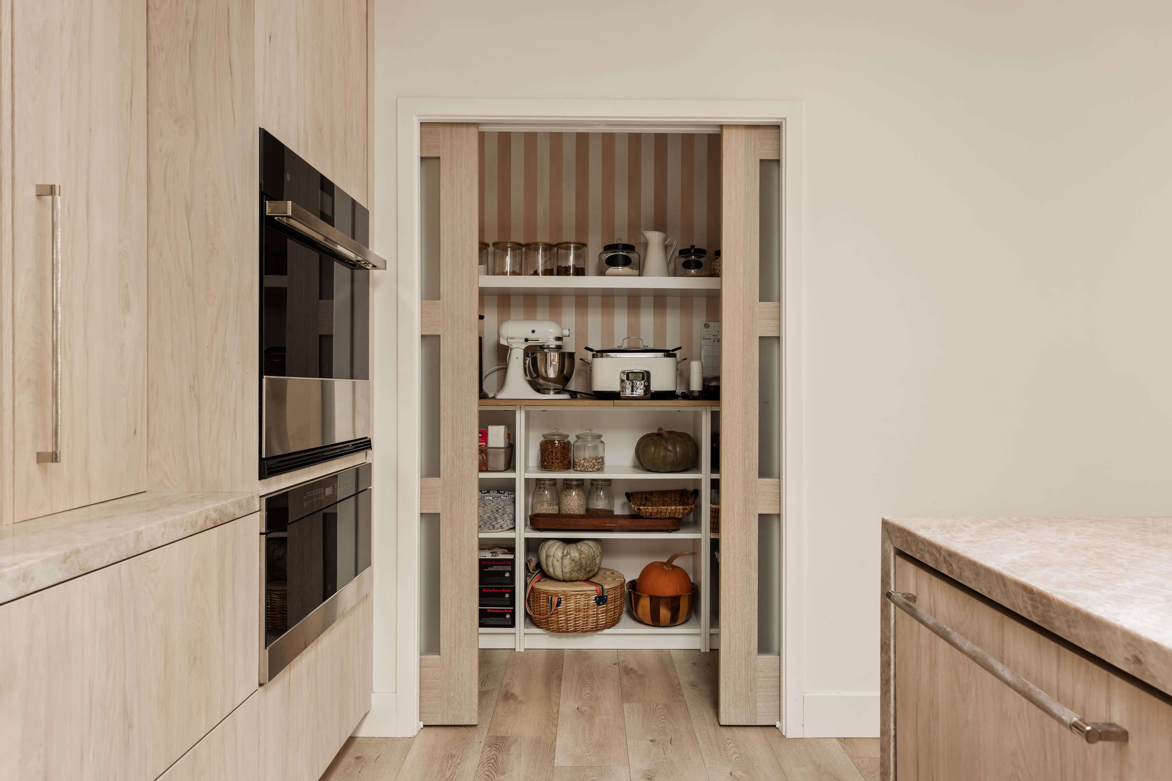 A pantry with open shelves and organized kitchen items is visible through sliding doors in a modern kitchen.