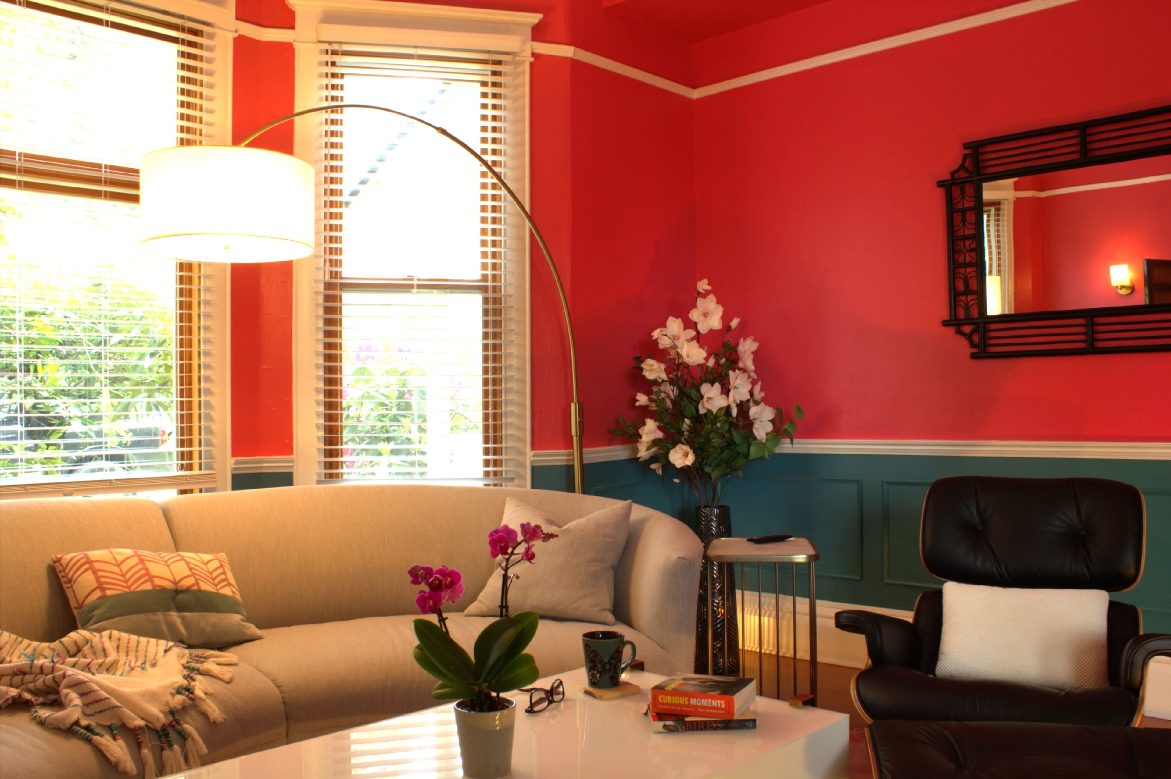 The image shows a brightly colored living room with a stylish sofa, a large floor lamp, and decorative flowers on a table.