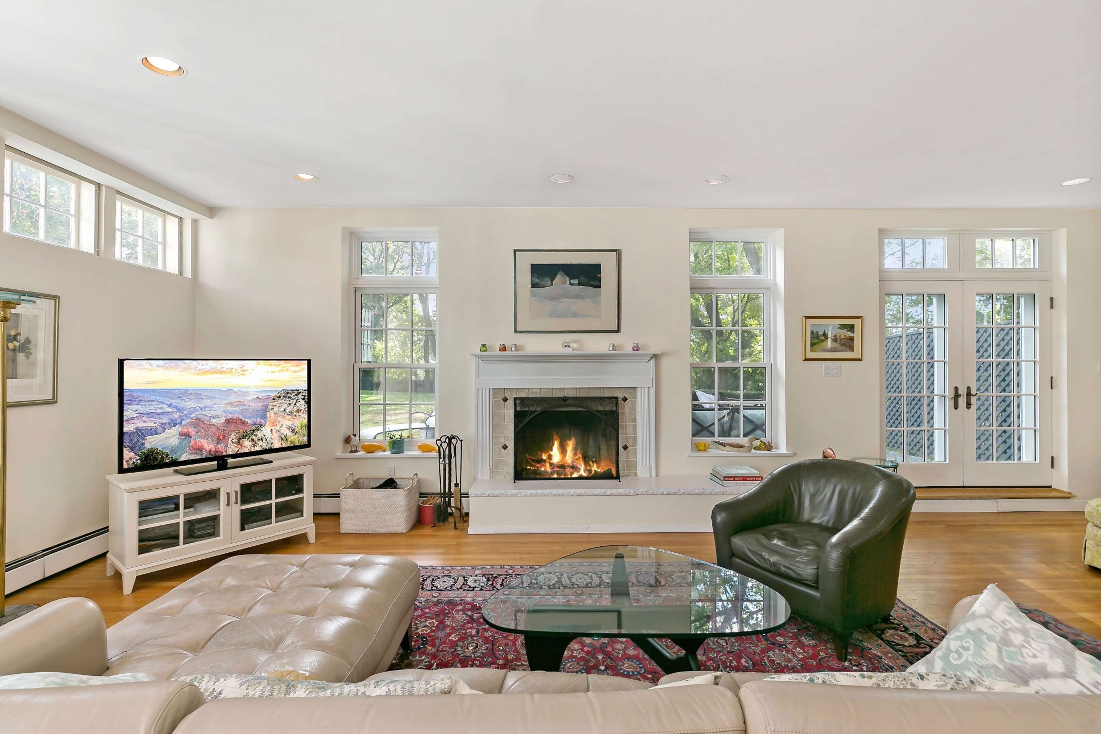 The living room features a fireplace, a large television, a sectional sofa, and several windows allowing natural light.