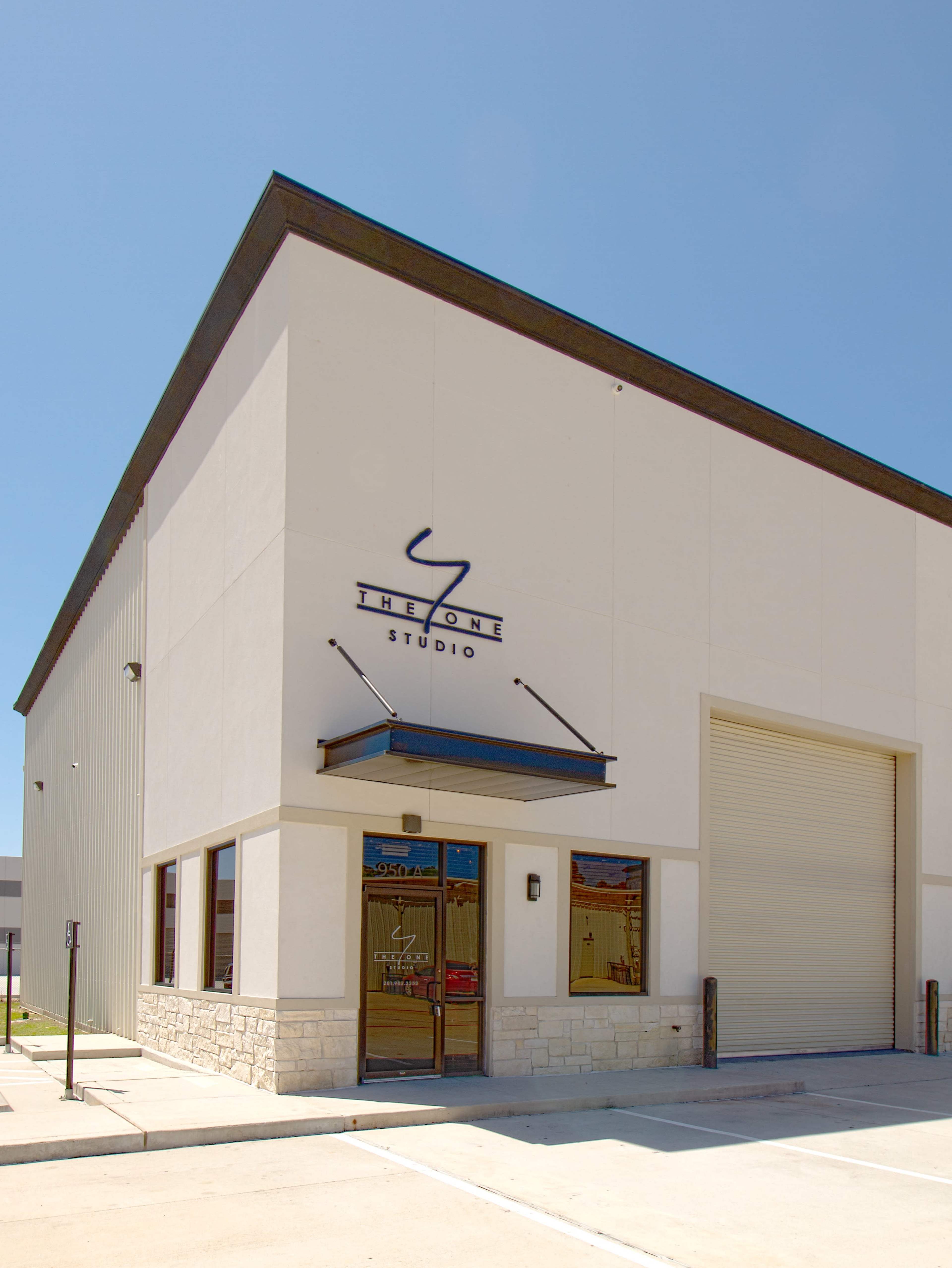 A modern, single-story studio building with a sign that reads "THE ONE STUDIO" above the entrance and a large roll-up door on one side.
