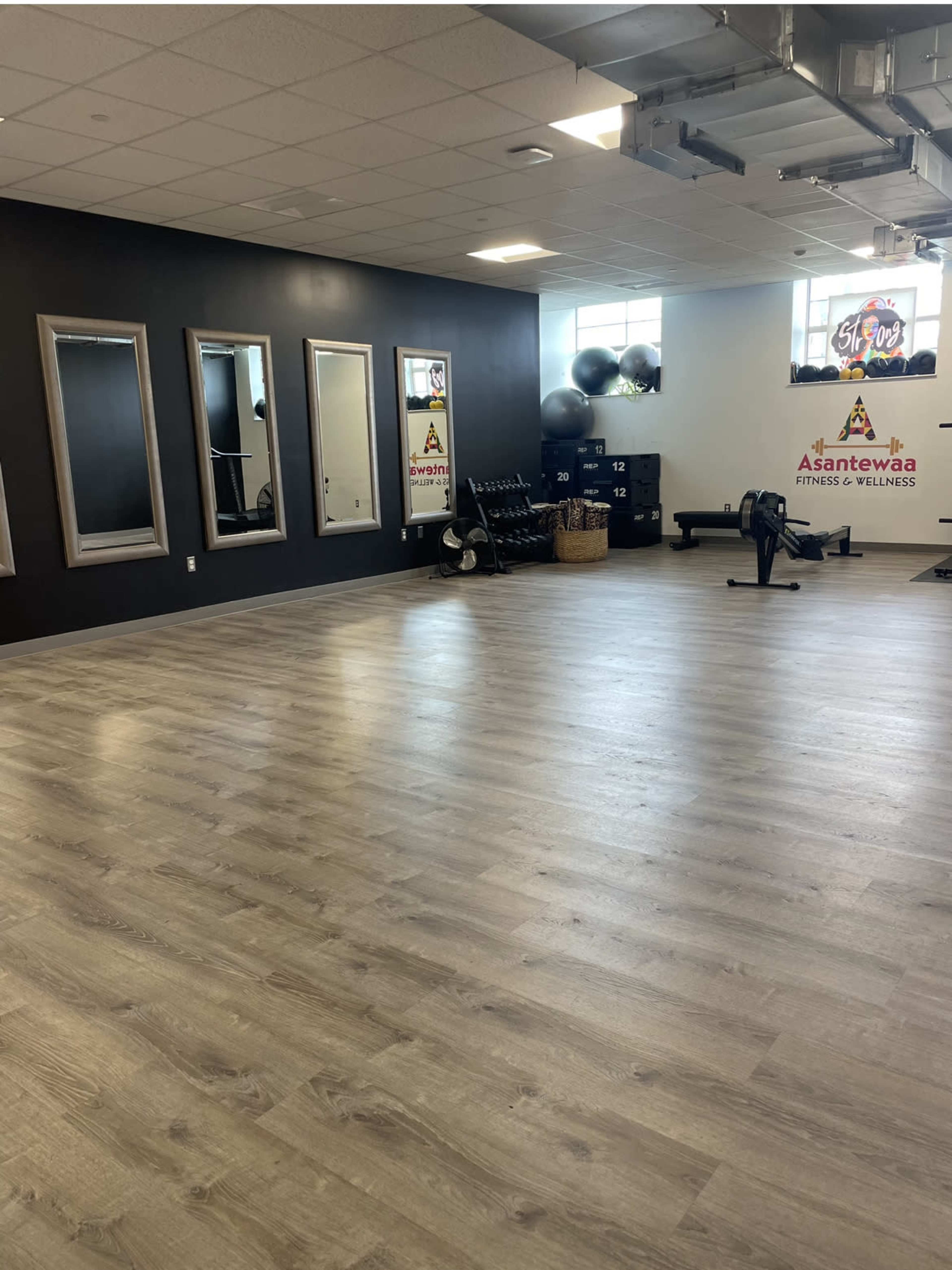 A spacious fitness studio with wooden flooring, large mirrors, exercise equipment, and fitness accessories neatly arranged against the walls.