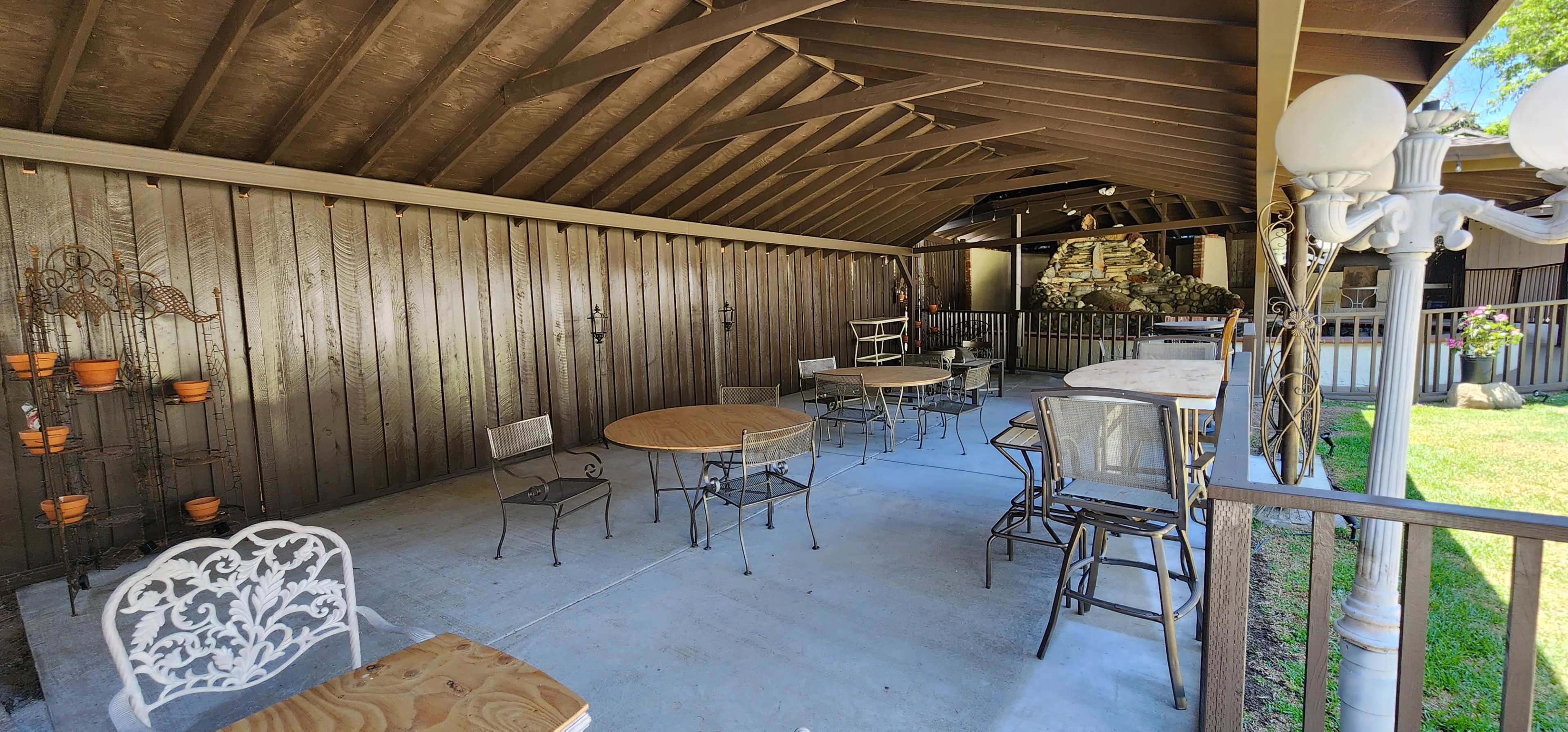 A covered patio with several tables and chairs arranged on a concrete floor.