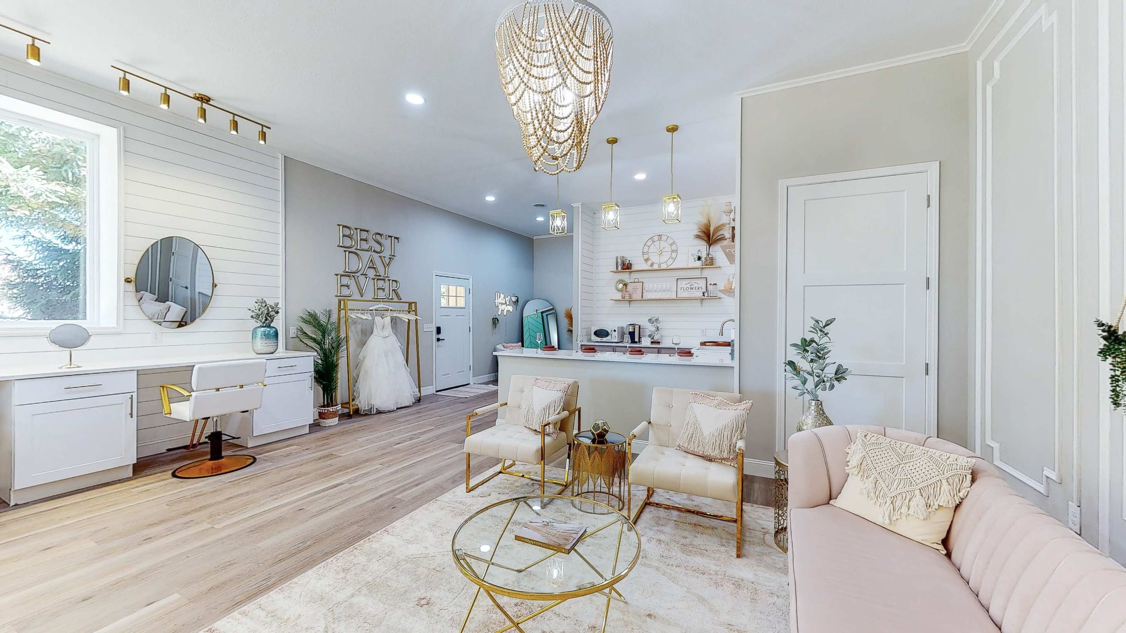 A modern interior space featuring a living area with two armchairs, a coffee table, and a decorative wall with the text "BEST DAY EVER," along with a vanity and kitchen area in the background.