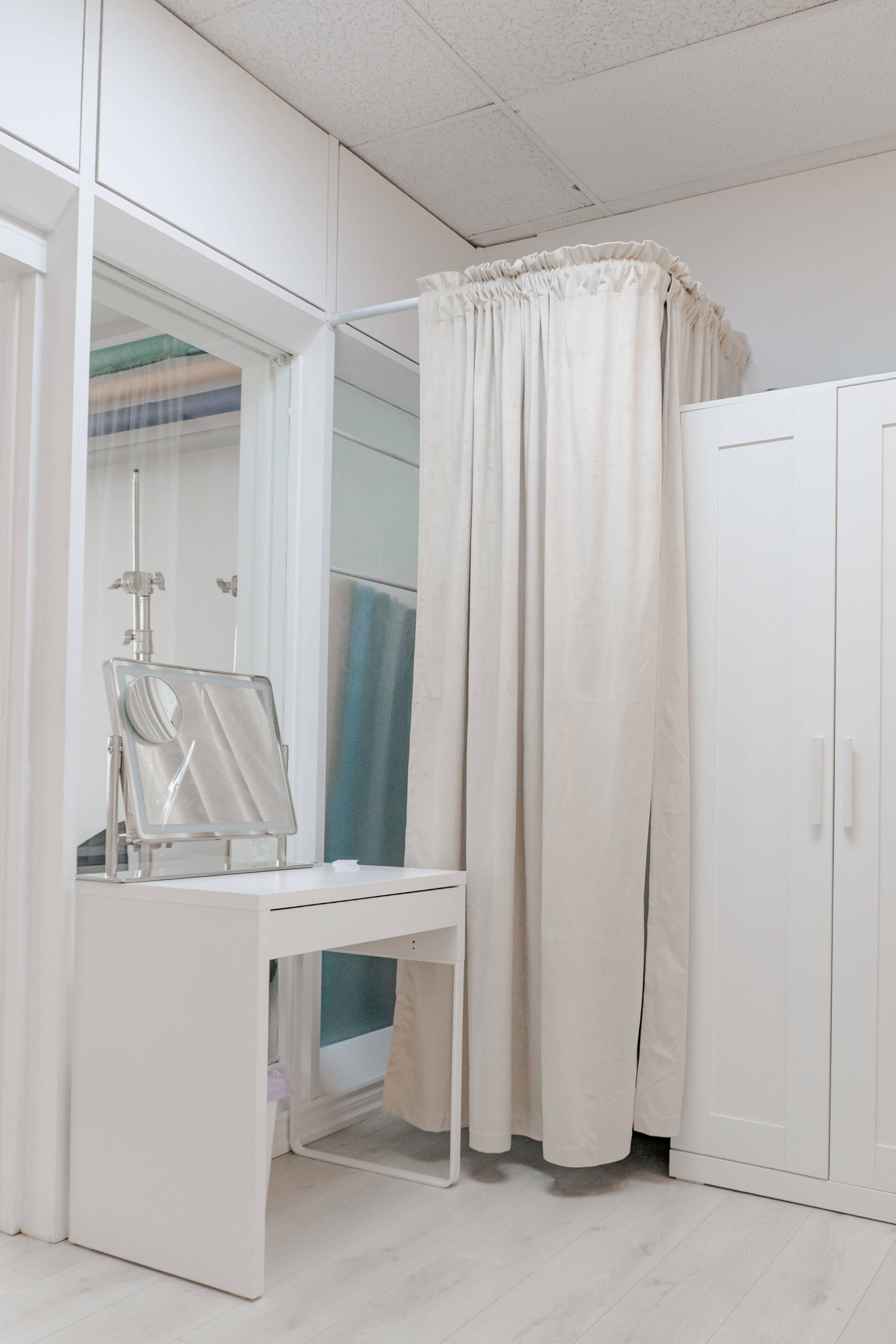 The image shows a small room featuring a white dressing area with a mirror on a table and a draped curtain that divides the space.