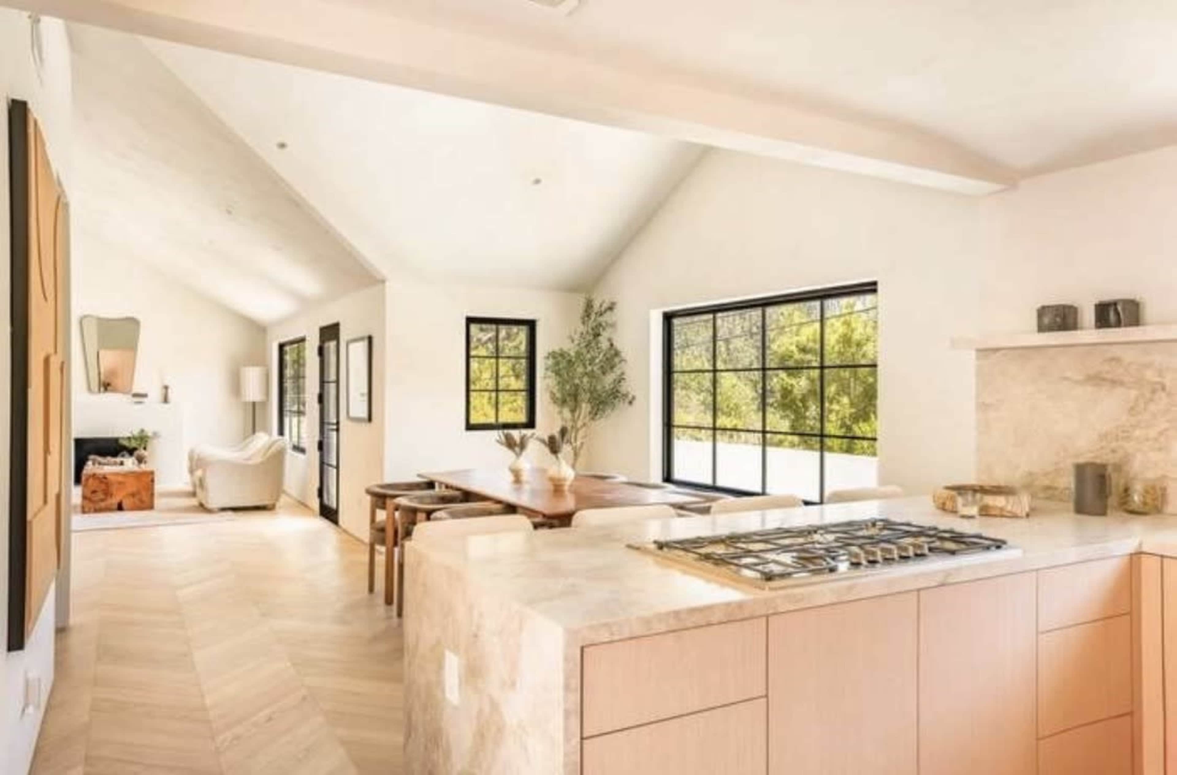 The image shows a modern kitchen with a gas stove, a dining area, and large windows allowing natural light to fill the space.