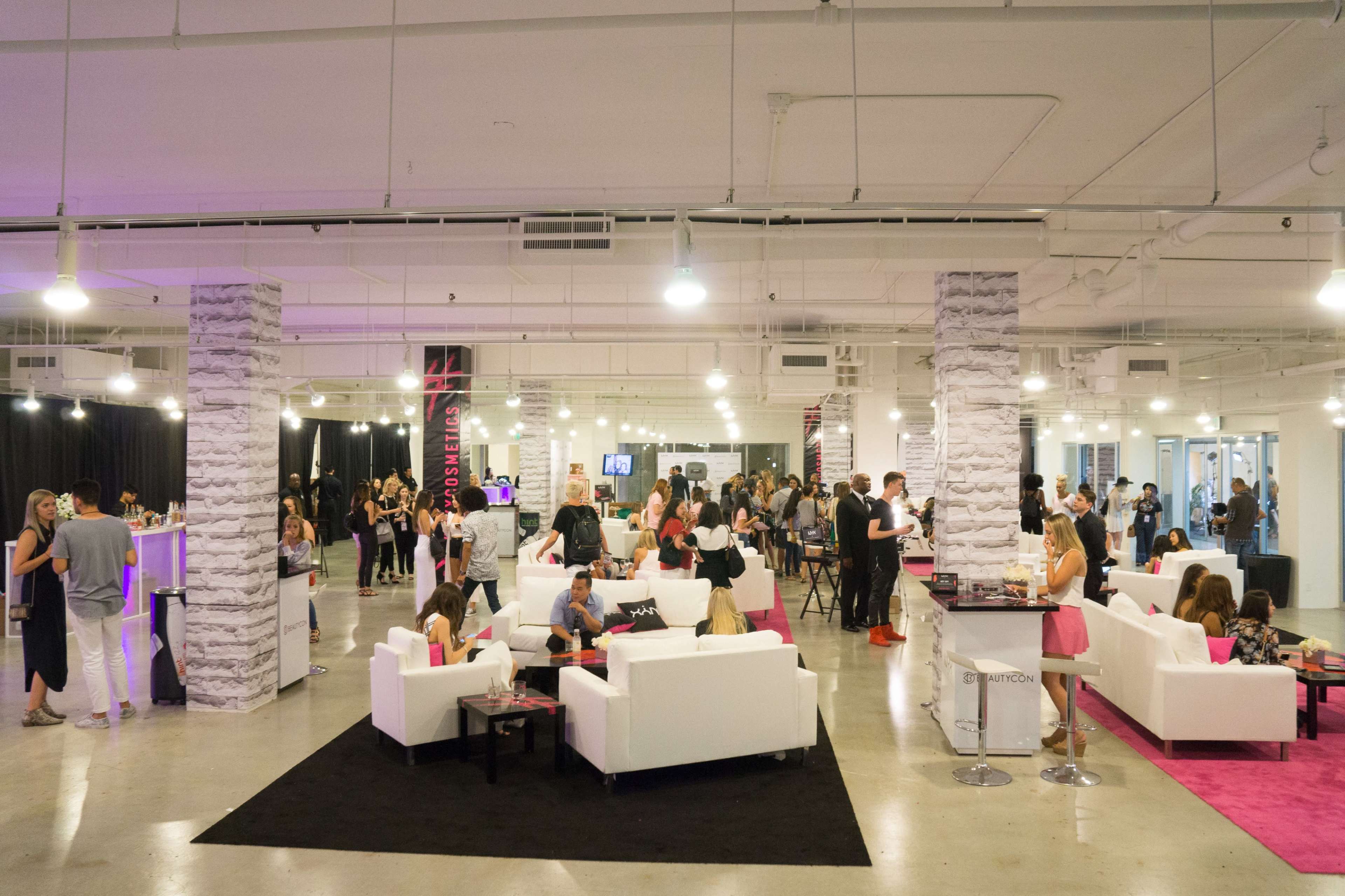 A spacious modern event venue features multiple seating areas and attendees engaged in various activities.