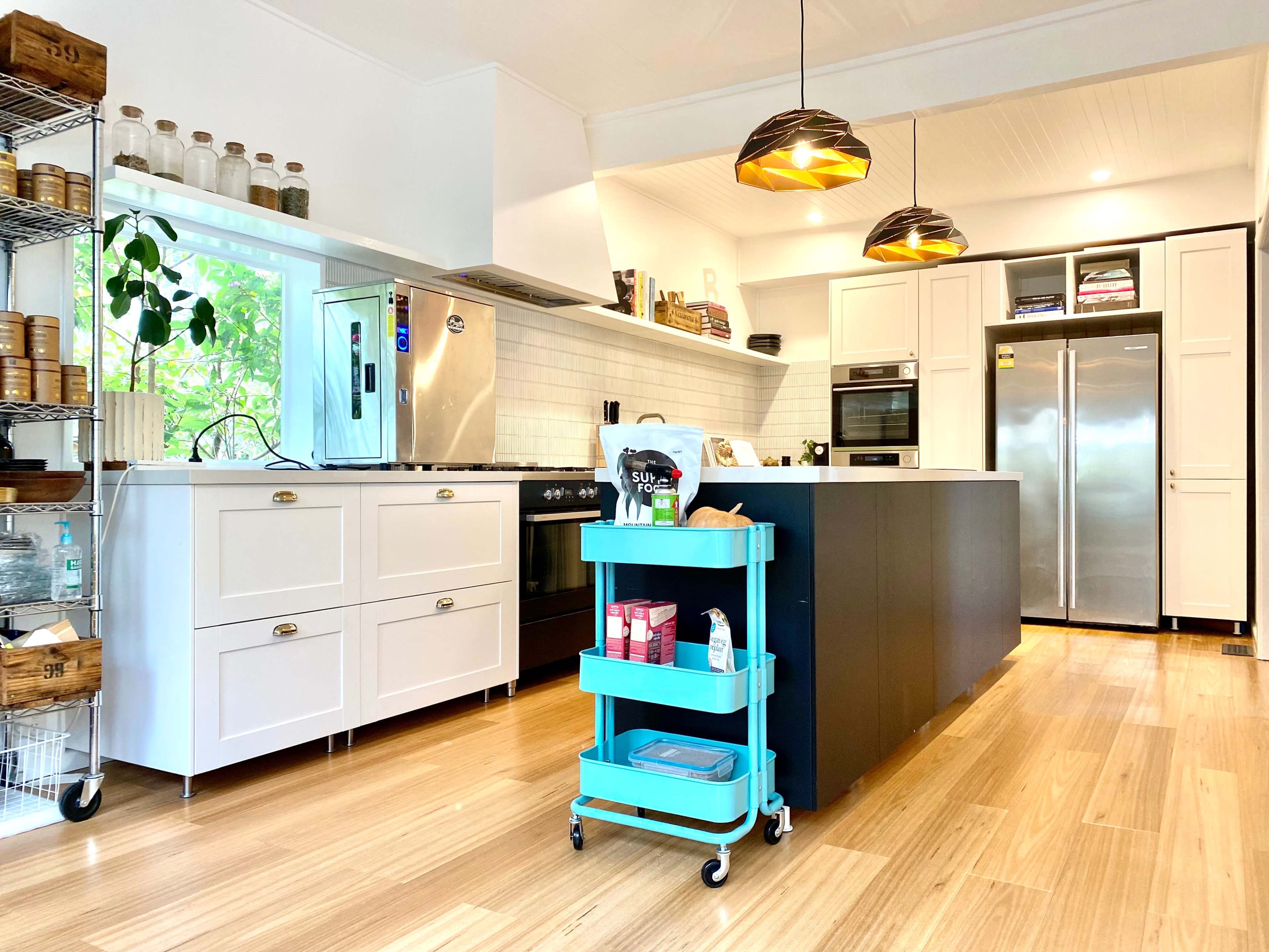 A modern kitchen with white cabinetry, stainless steel appliances, and a wooden floor, featuring an island with a food cart on wheels.