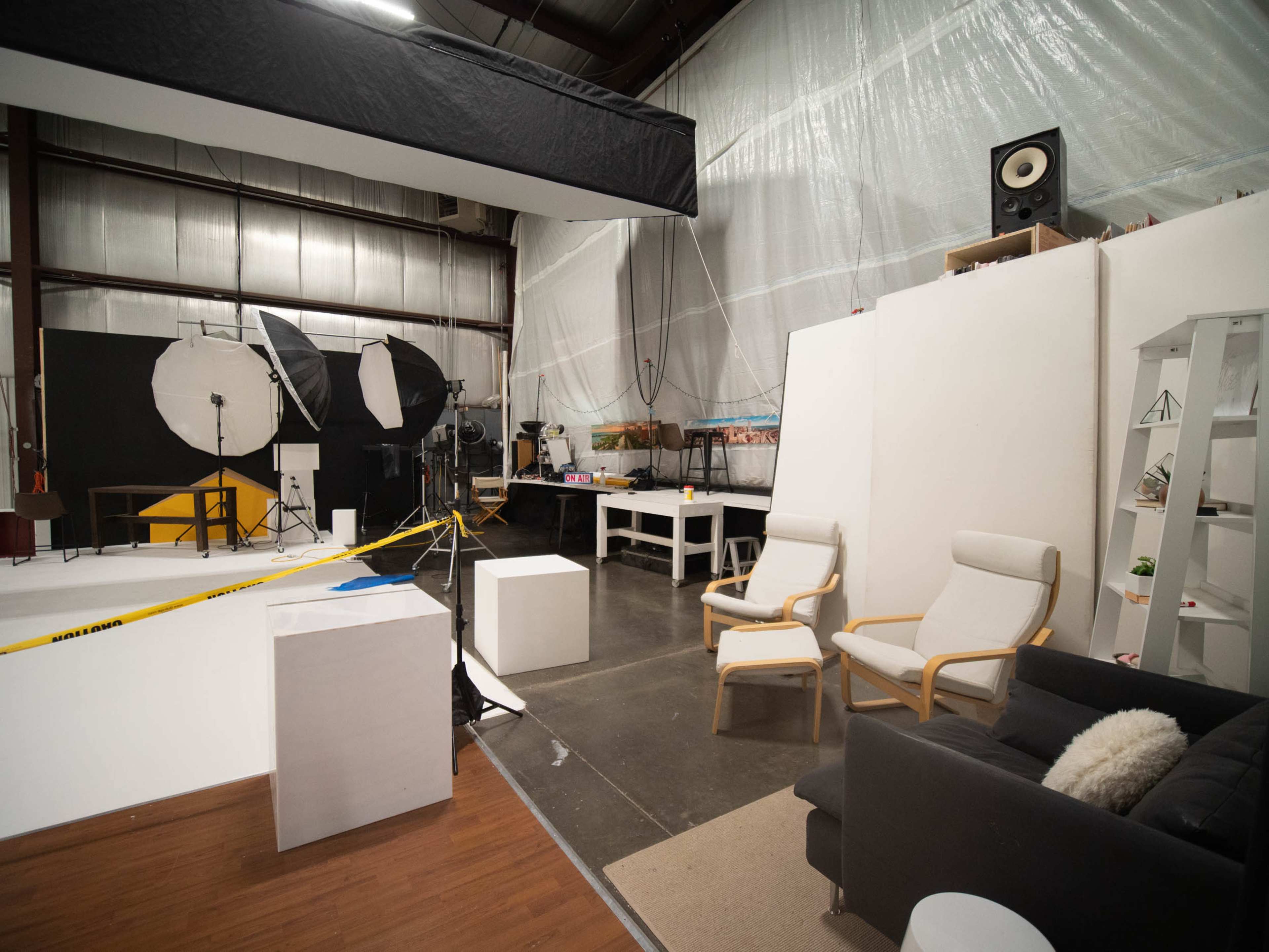 A photography studio with various lighting setups, a work area, and seating arranged against a white backdrop.
