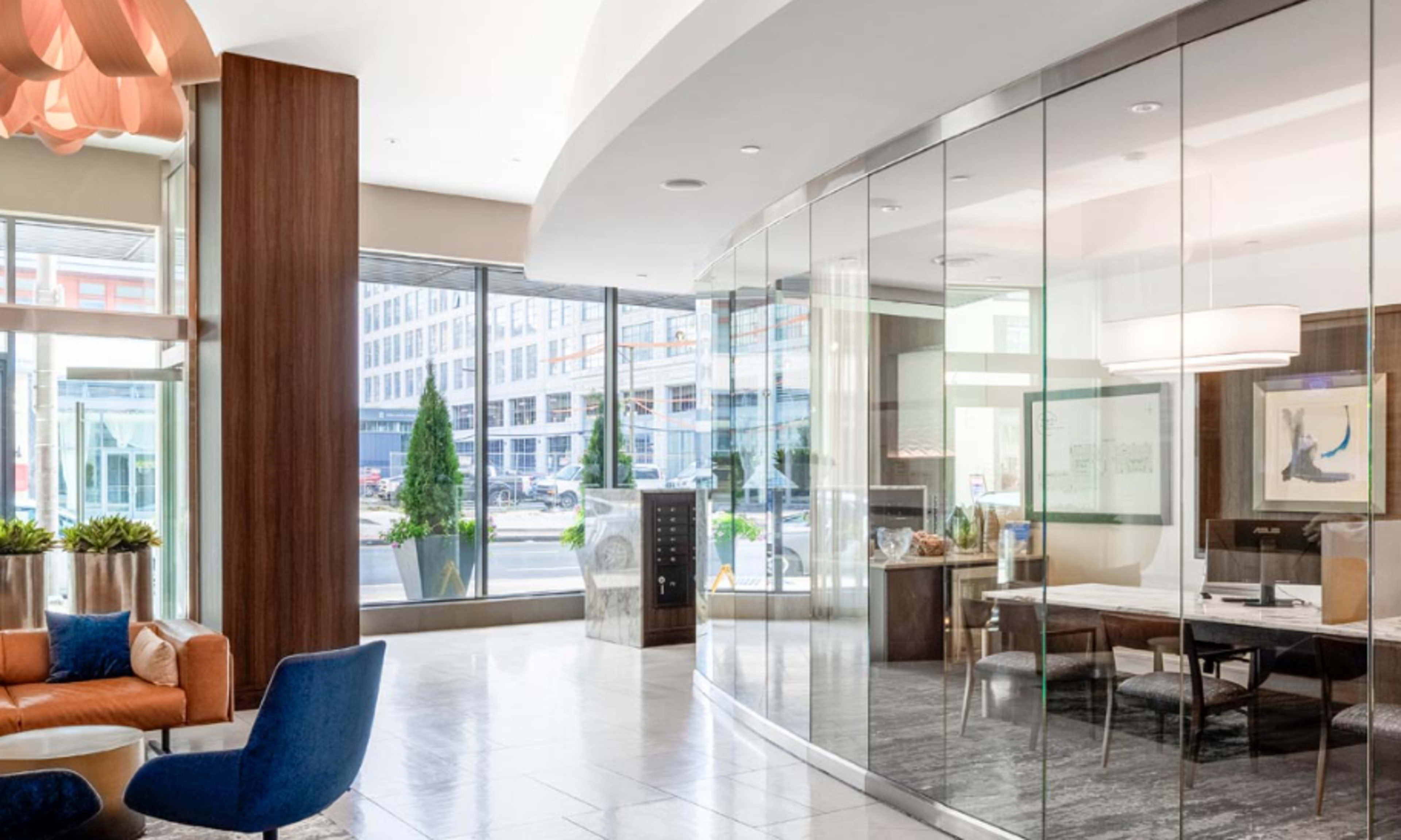 The image shows a sleek, modern lobby with large windows, contemporary furniture, and a glass-walled meeting room.