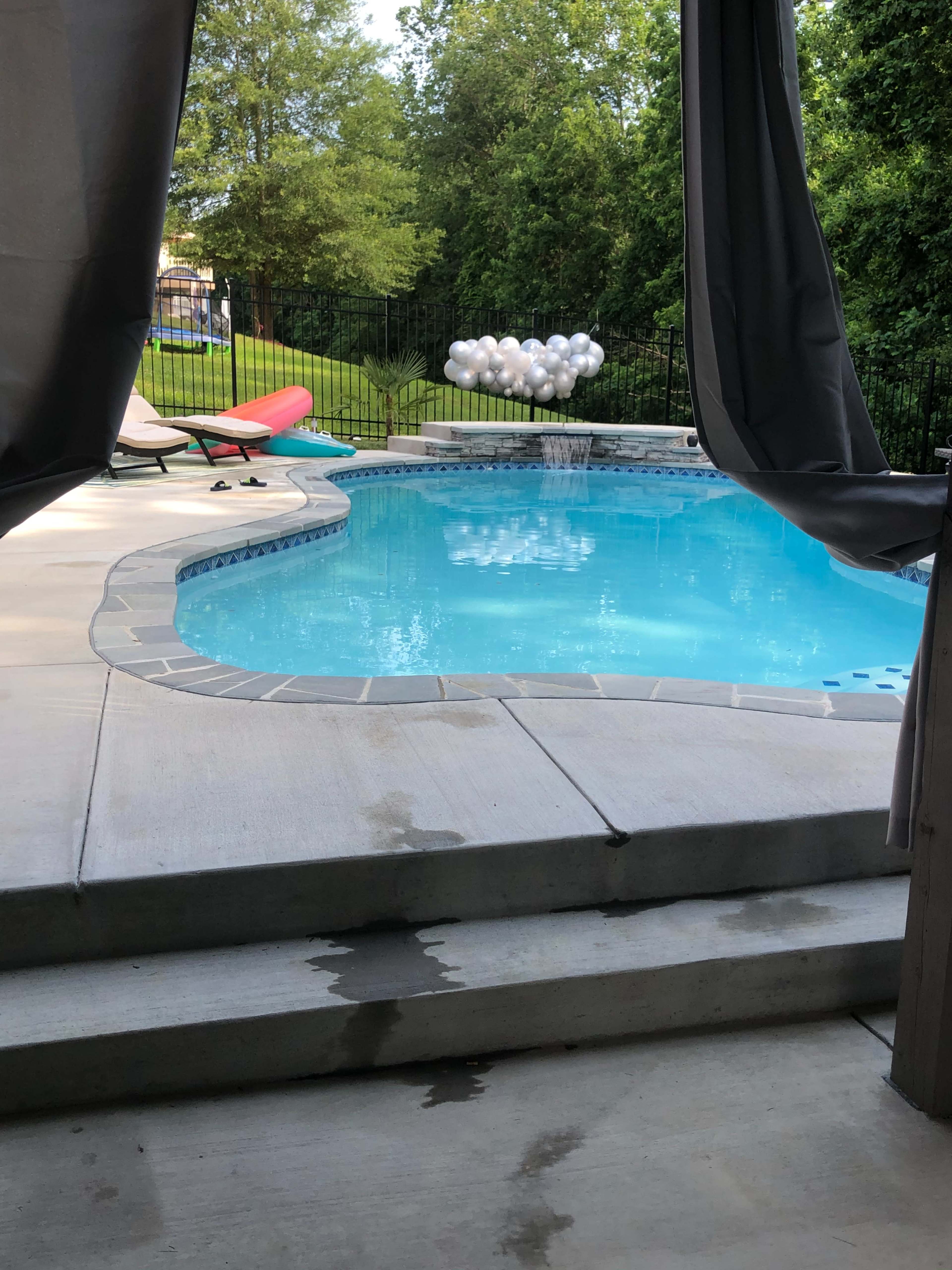 A swimming pool is visible through a covered patio area, surrounded by lounge chairs and a cluster of balloons in the background.