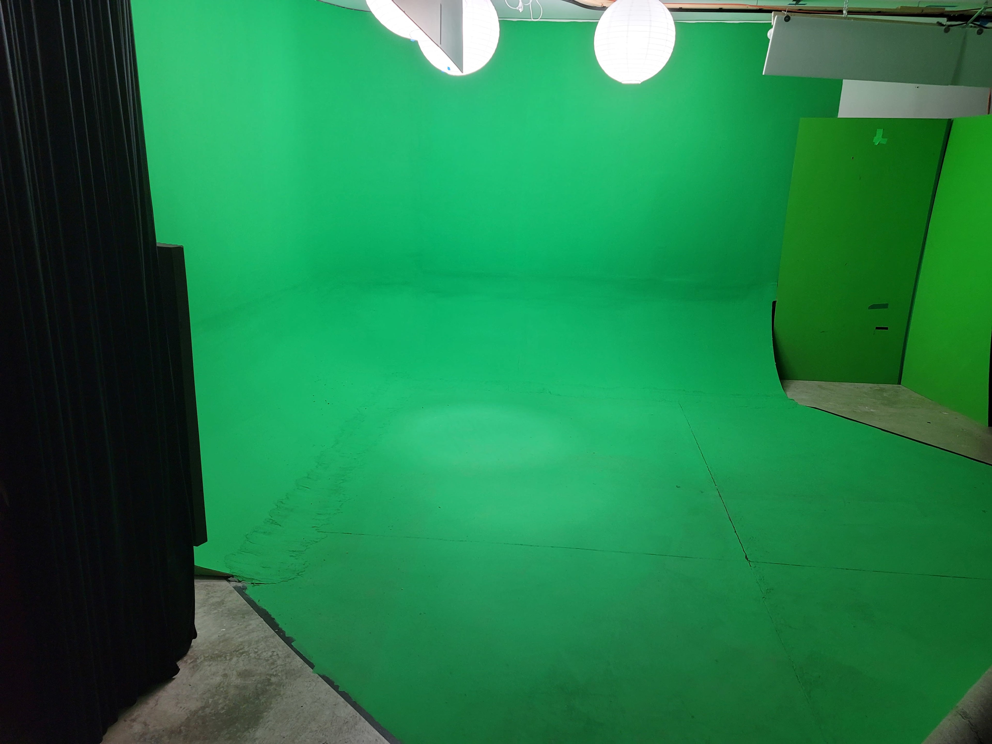The image shows a green screen studio with smooth green walls and flooring, illuminated by round lantern lights.