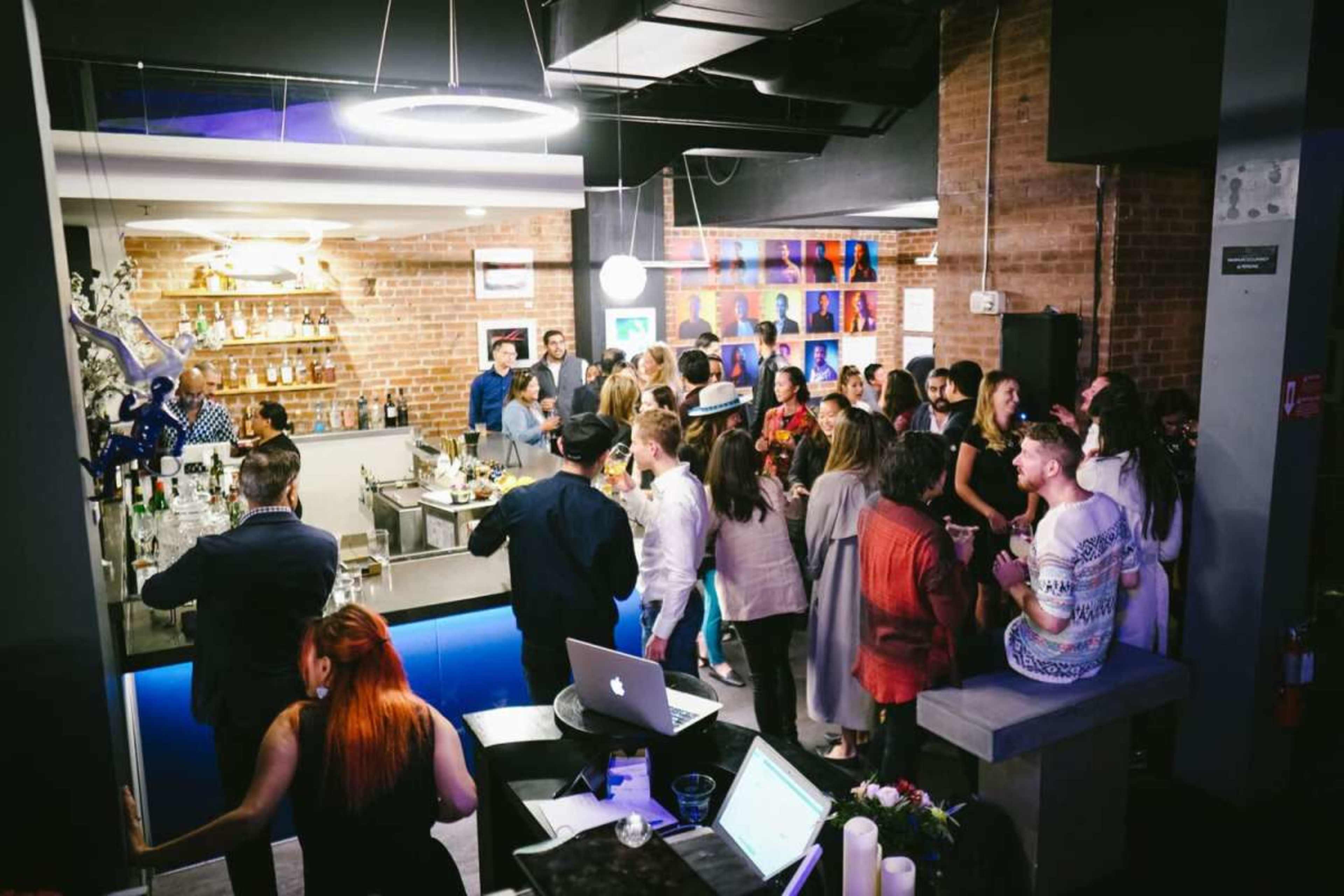 A crowded bar scene features a mix of people socializing and enjoying drinks at a well-lit establishment with a modern design.