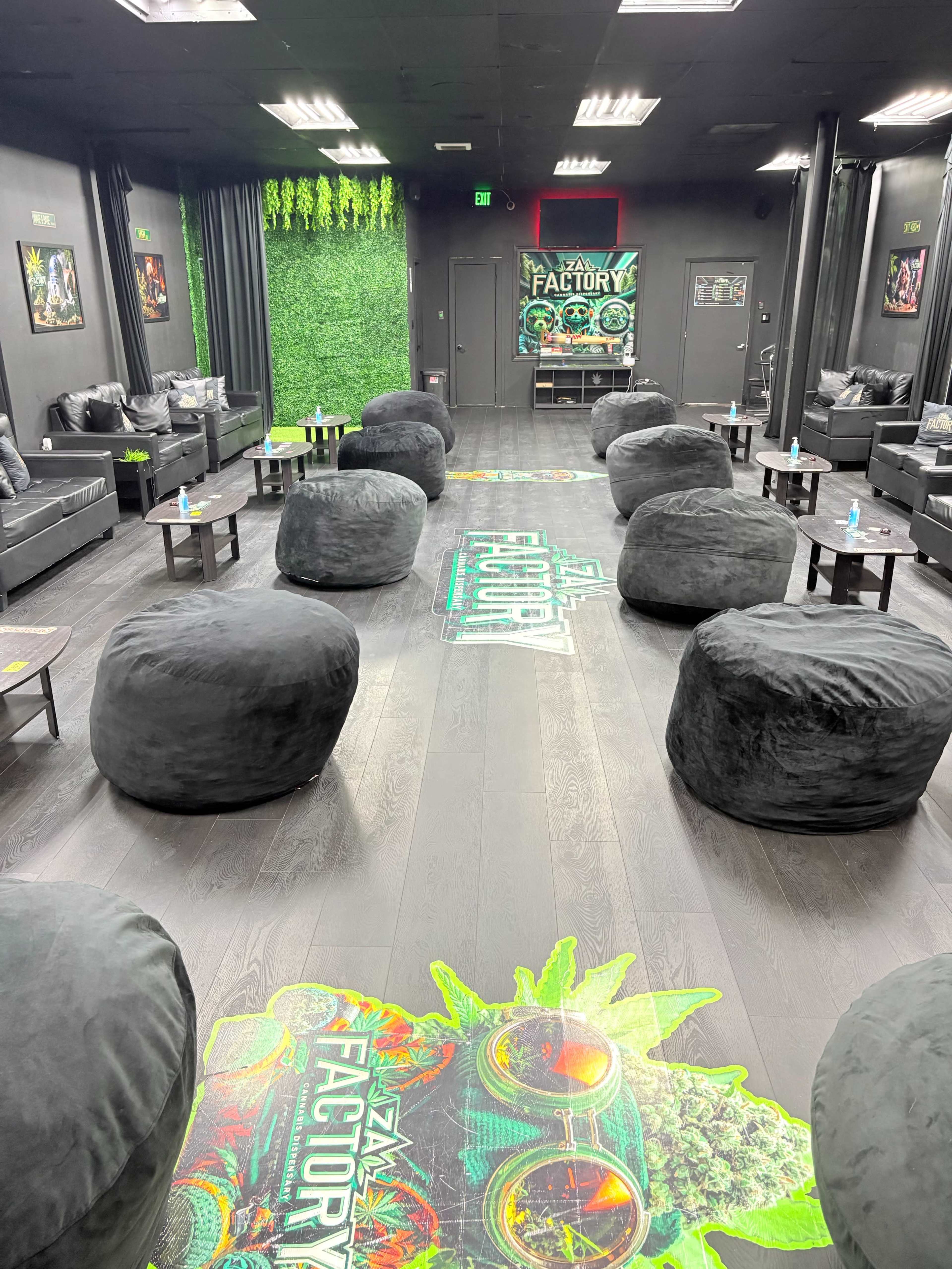The image shows a modern lounge area furnished with black bean bag chairs and decorated with vibrant artwork and greenery on the walls.