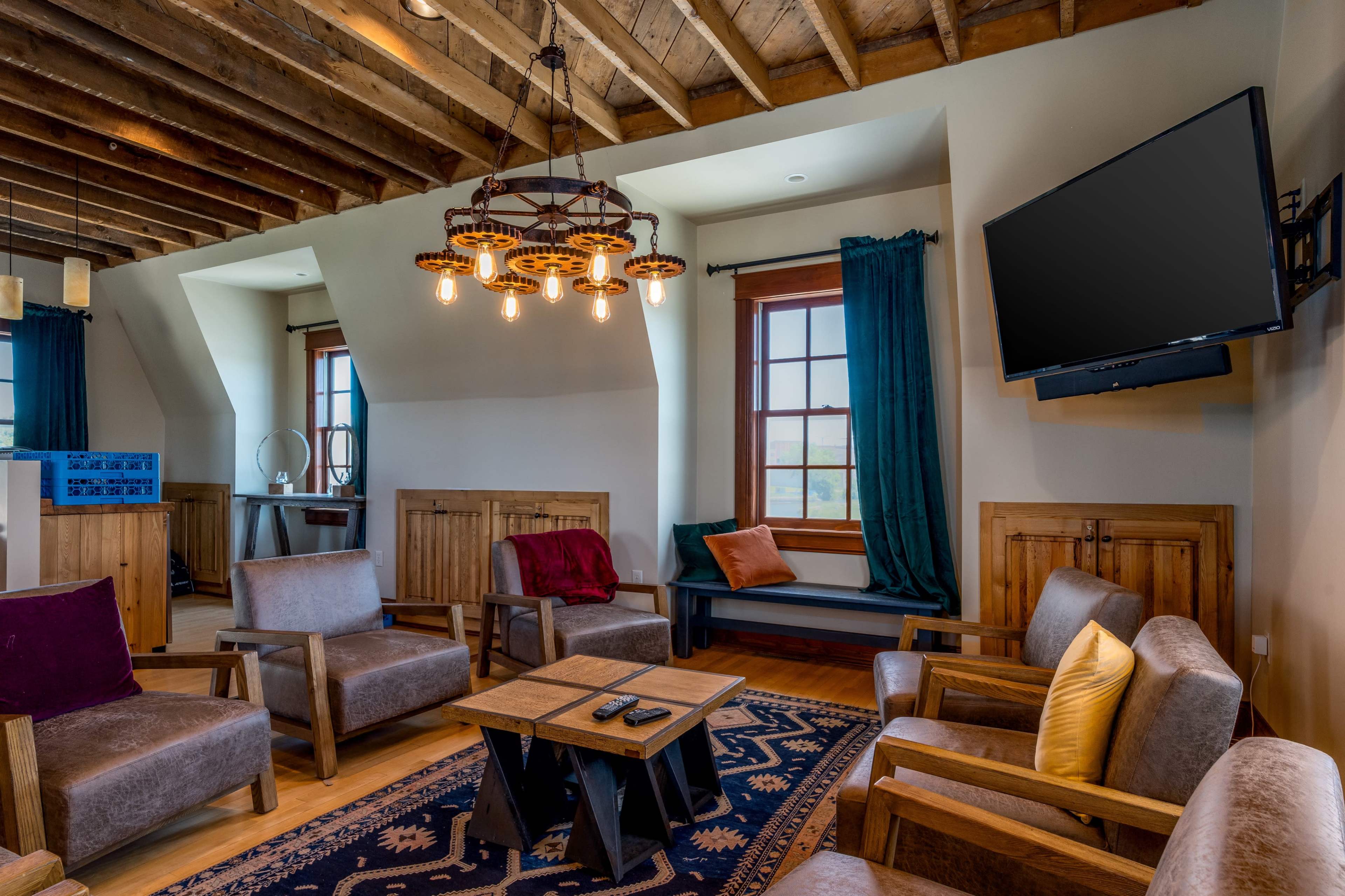 A cozy lounge area with wooden furniture, a central table, and a large television mounted on the wall under exposed wooden beams.