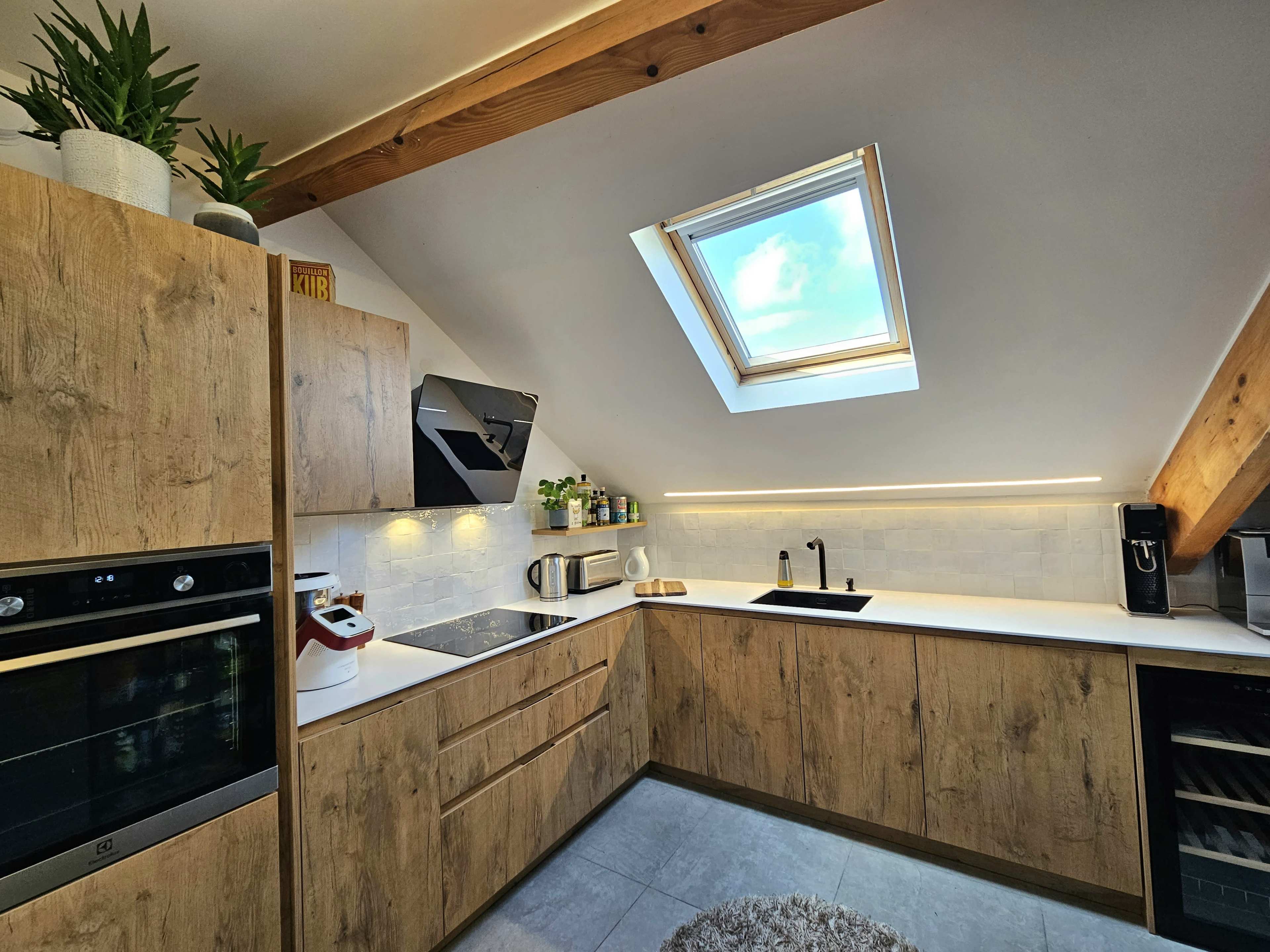 A modern kitchen with wooden cabinetry, a skylight, and sleek appliances under exposed beams.